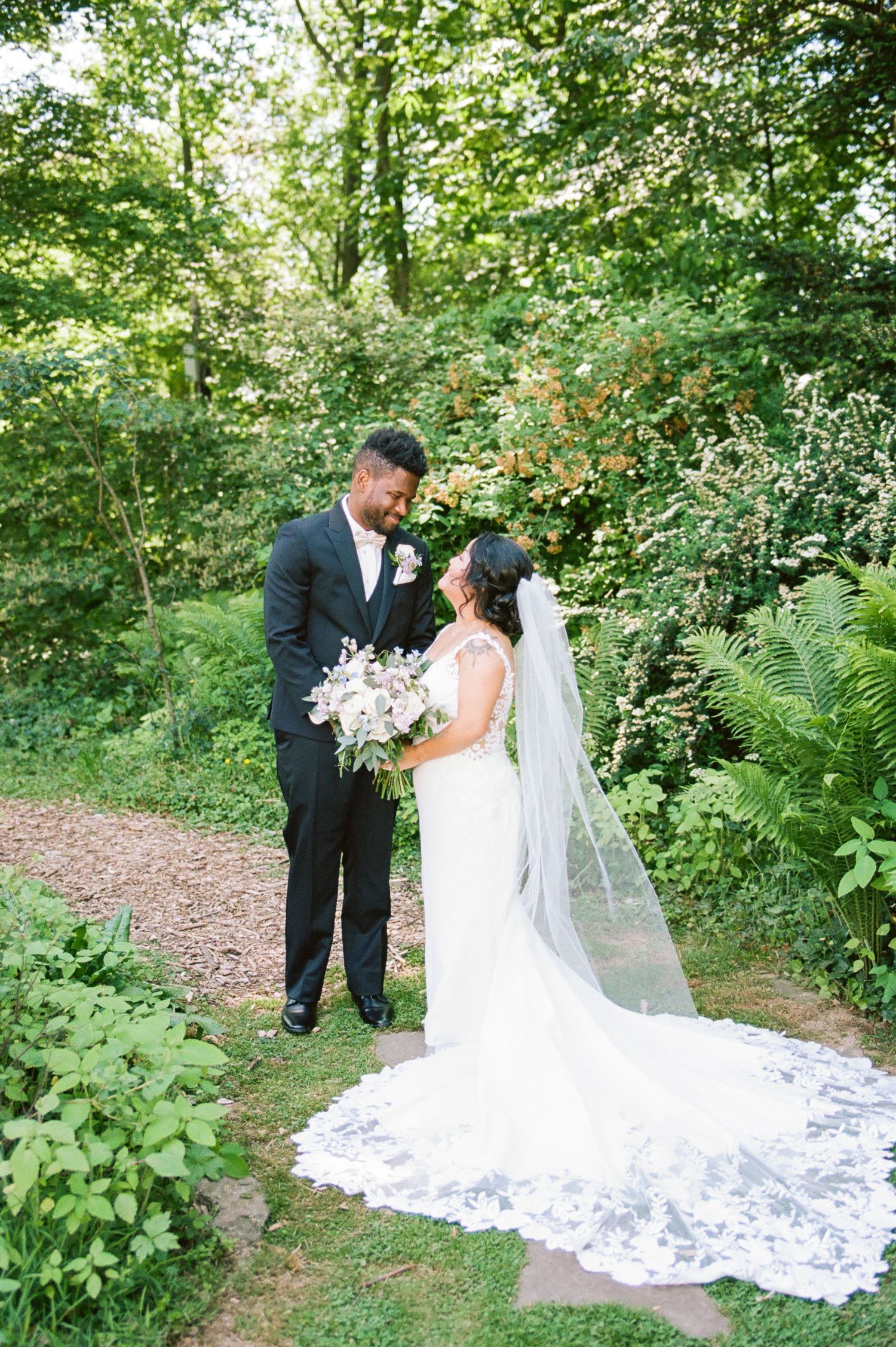 Wedding couple posing together on a garden path surrounded by greenery.