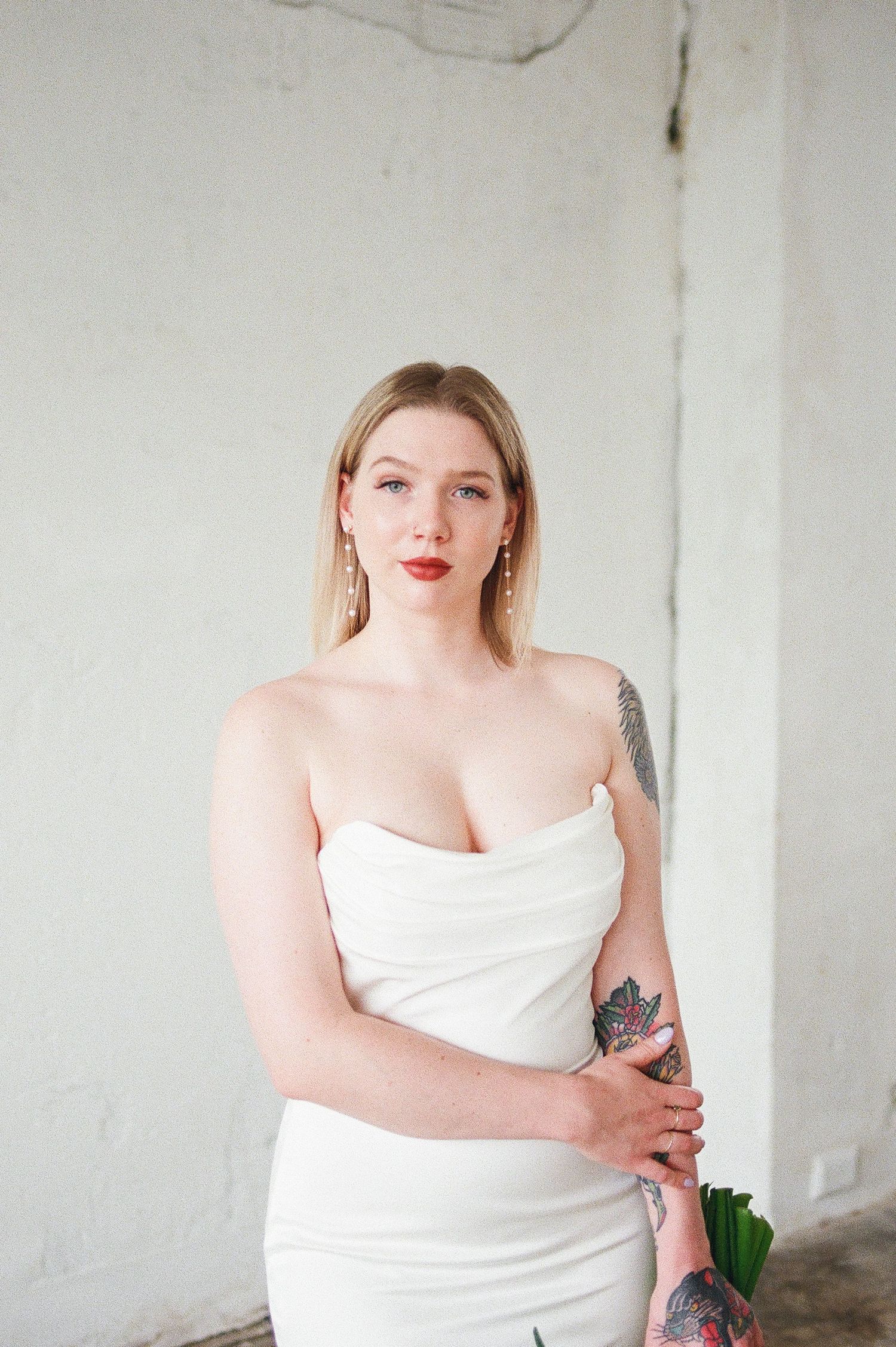 Intimate bridal portrait series in strapless white gown against white brick wall.