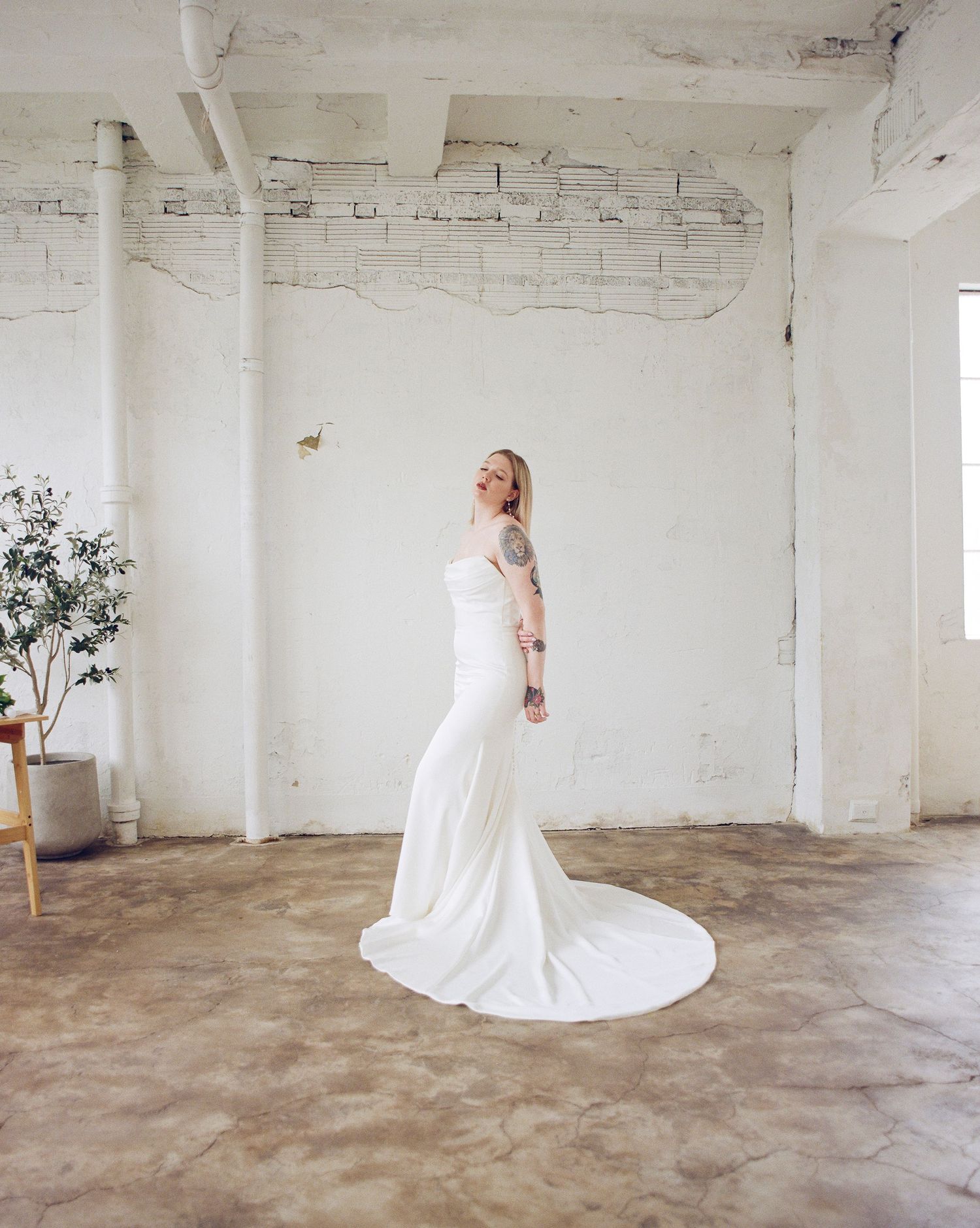 Full-length bridal portrait showing flowing train in minimalist white industrial setting.