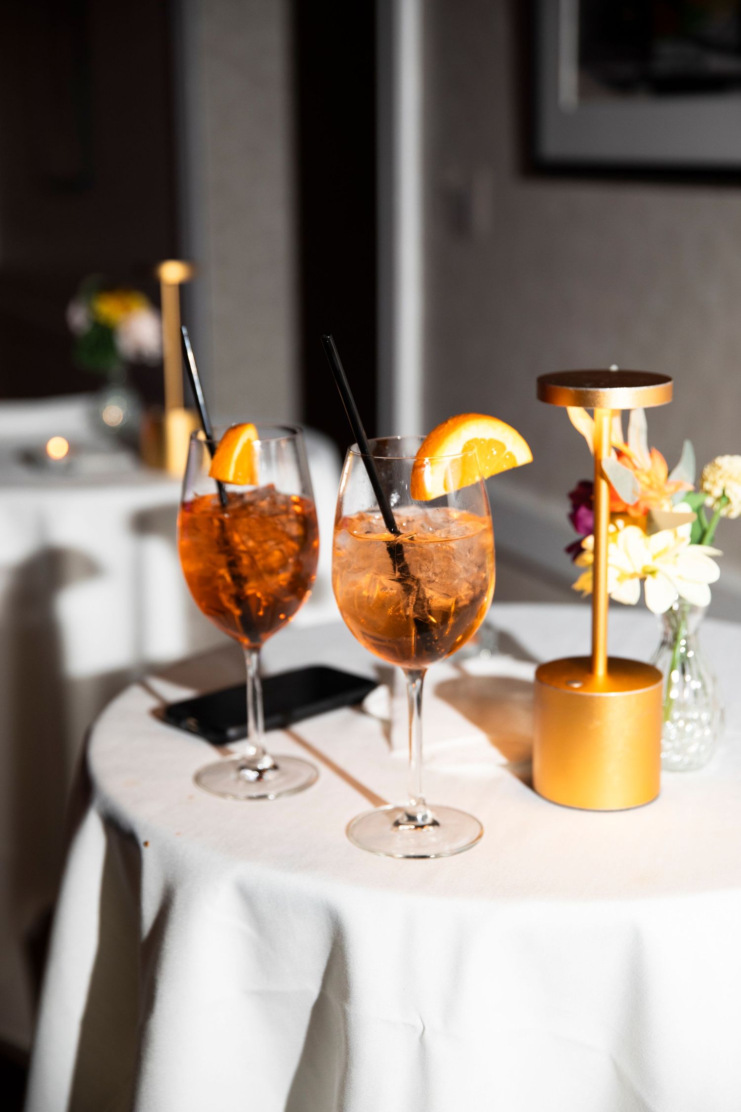 Cocktail glasses with orange garnishes on white tablecloth in romantic lighting.