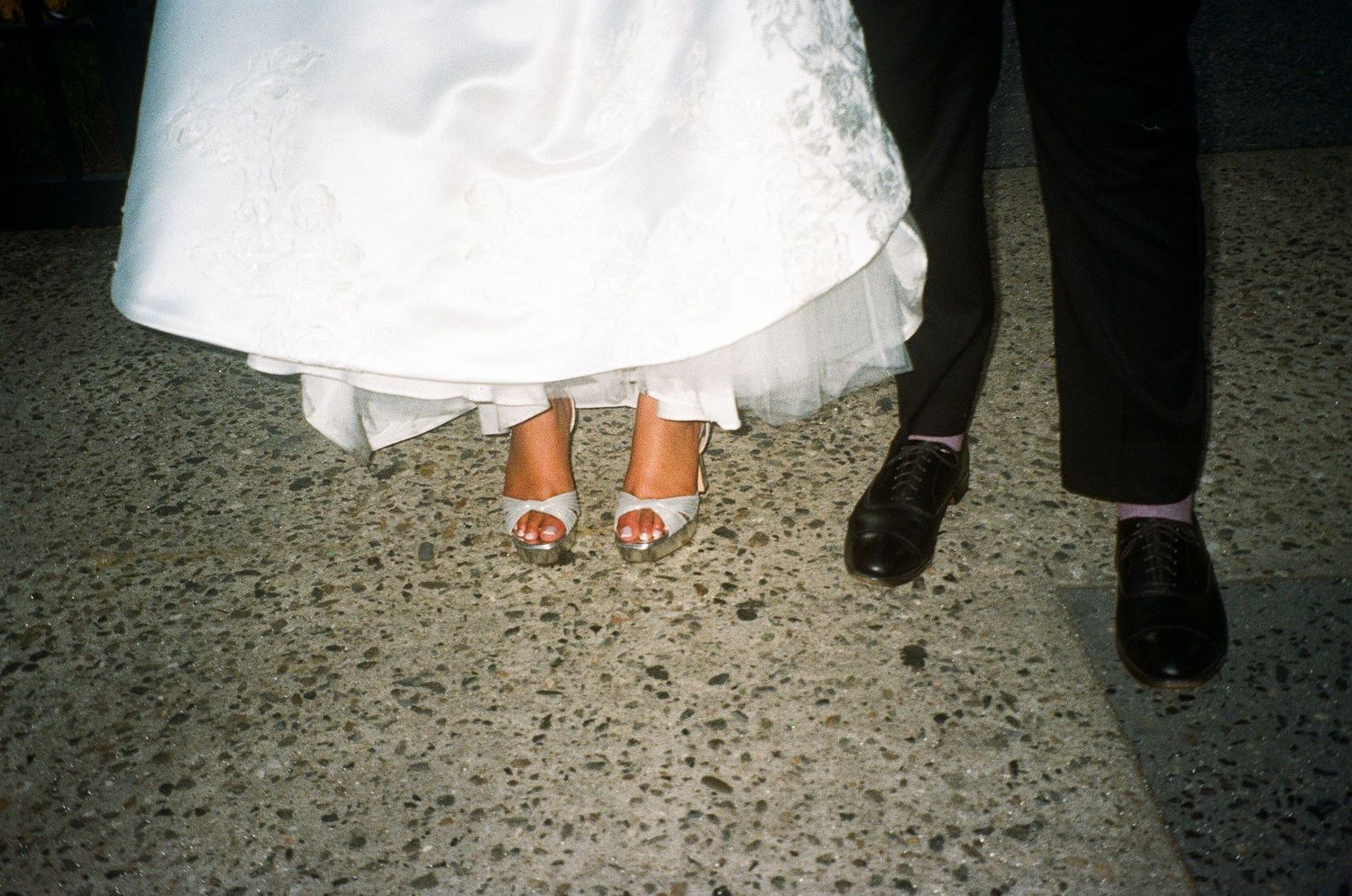 Wedding reception details showing white dress hemlines and formal shoes on a tiled floor.