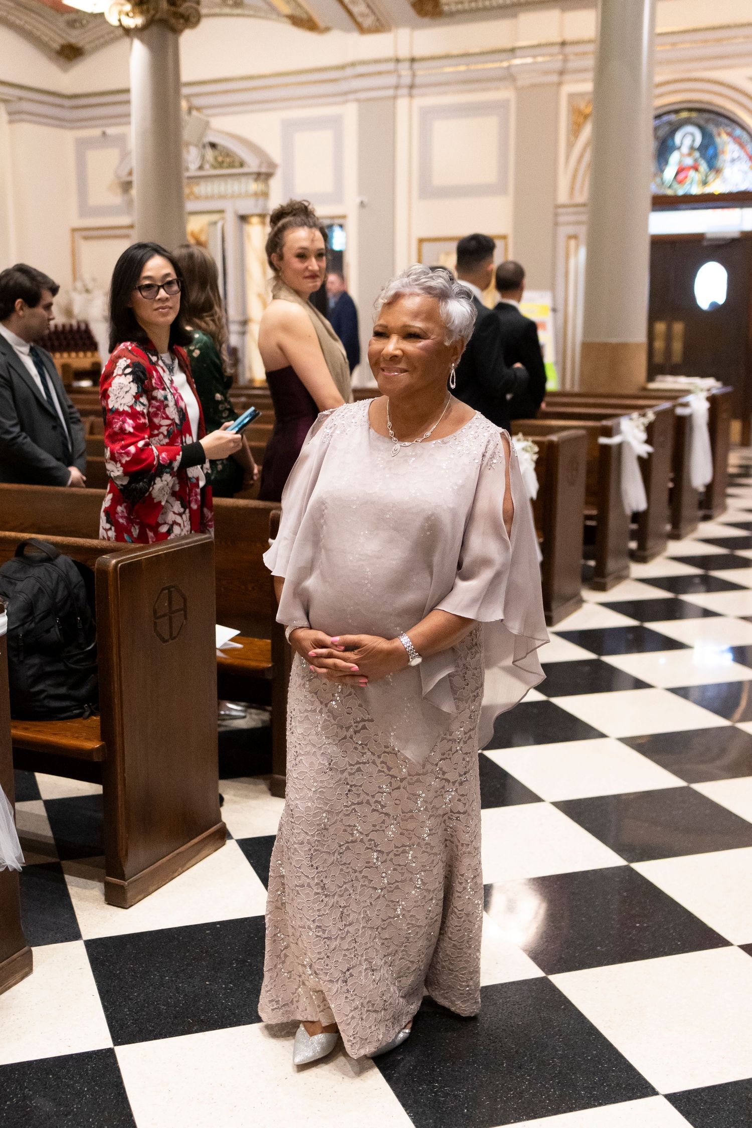 Wedding guests mingling in an elegant church interior with black and white checkered floor.