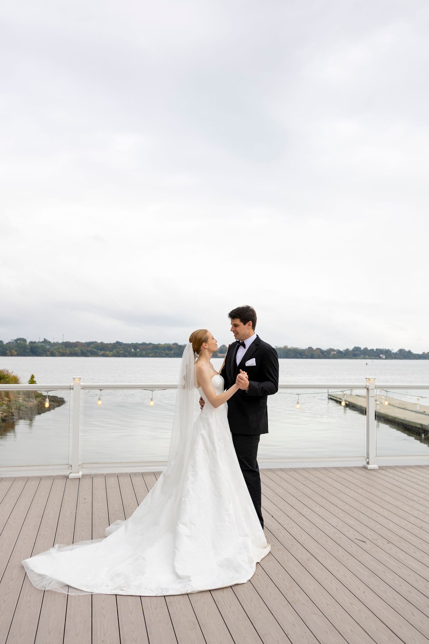 A romantic wedding photoshoot on a wooden deck overlooking a serene waterfront.