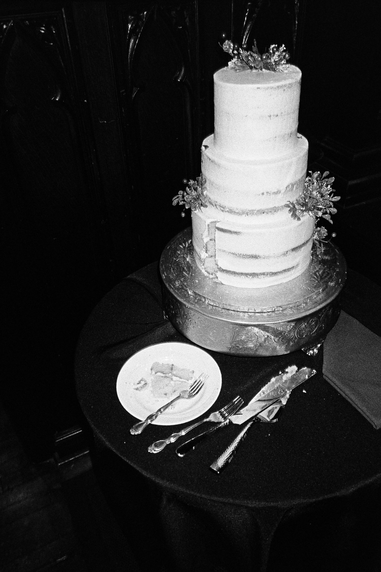 Simple white wedding cake displayed on dark table with serving utensils.