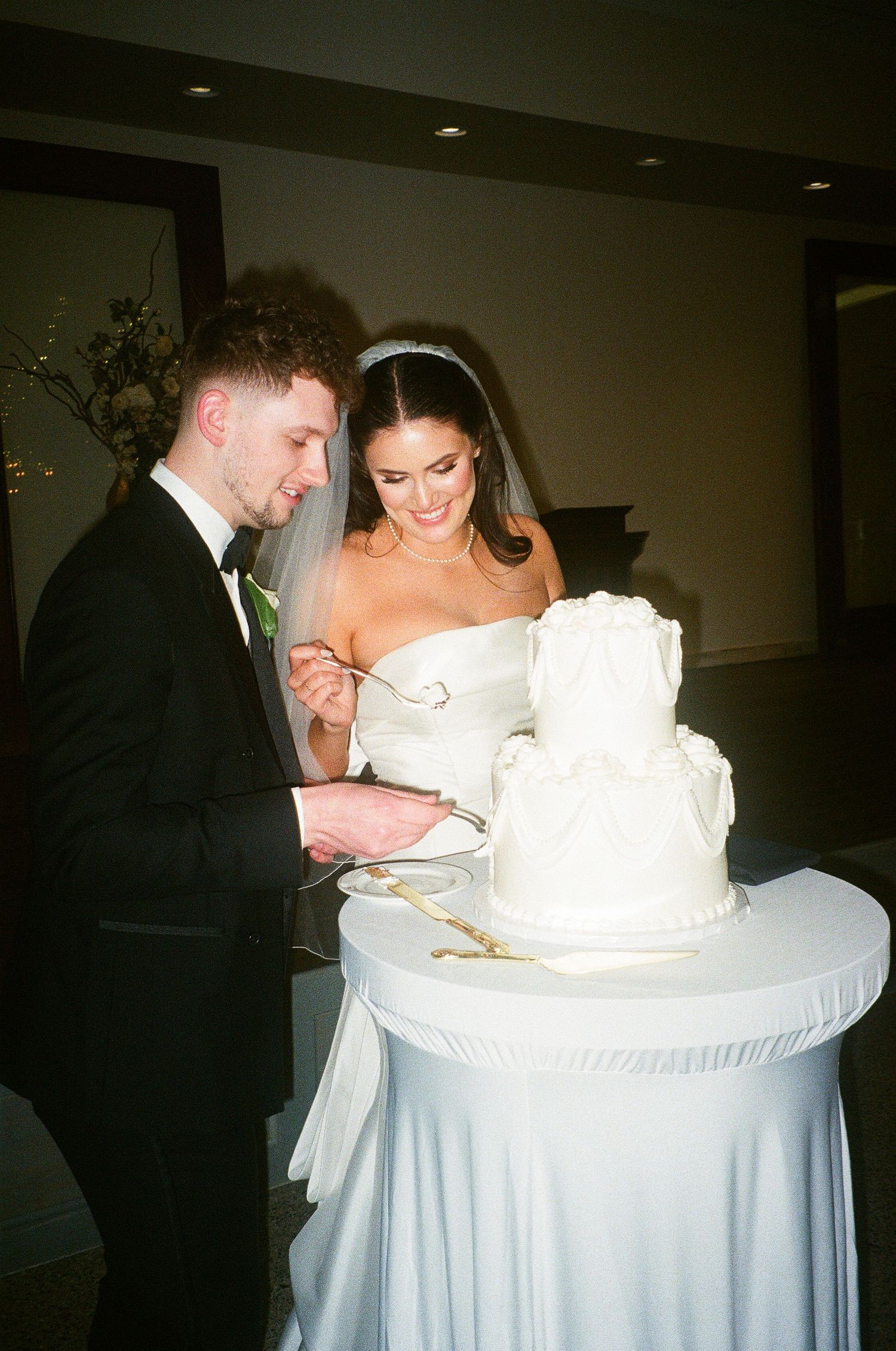 Bride and groom cutting their white tiered wedding cake together at their elegant wedding reception.