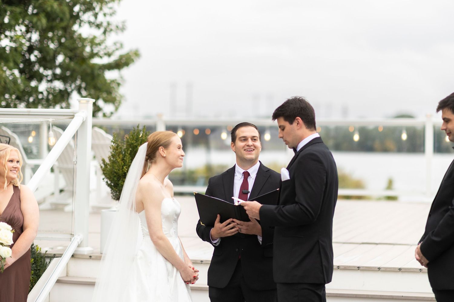 Wedding party members standing in a row during an outdoor waterfront ceremony.