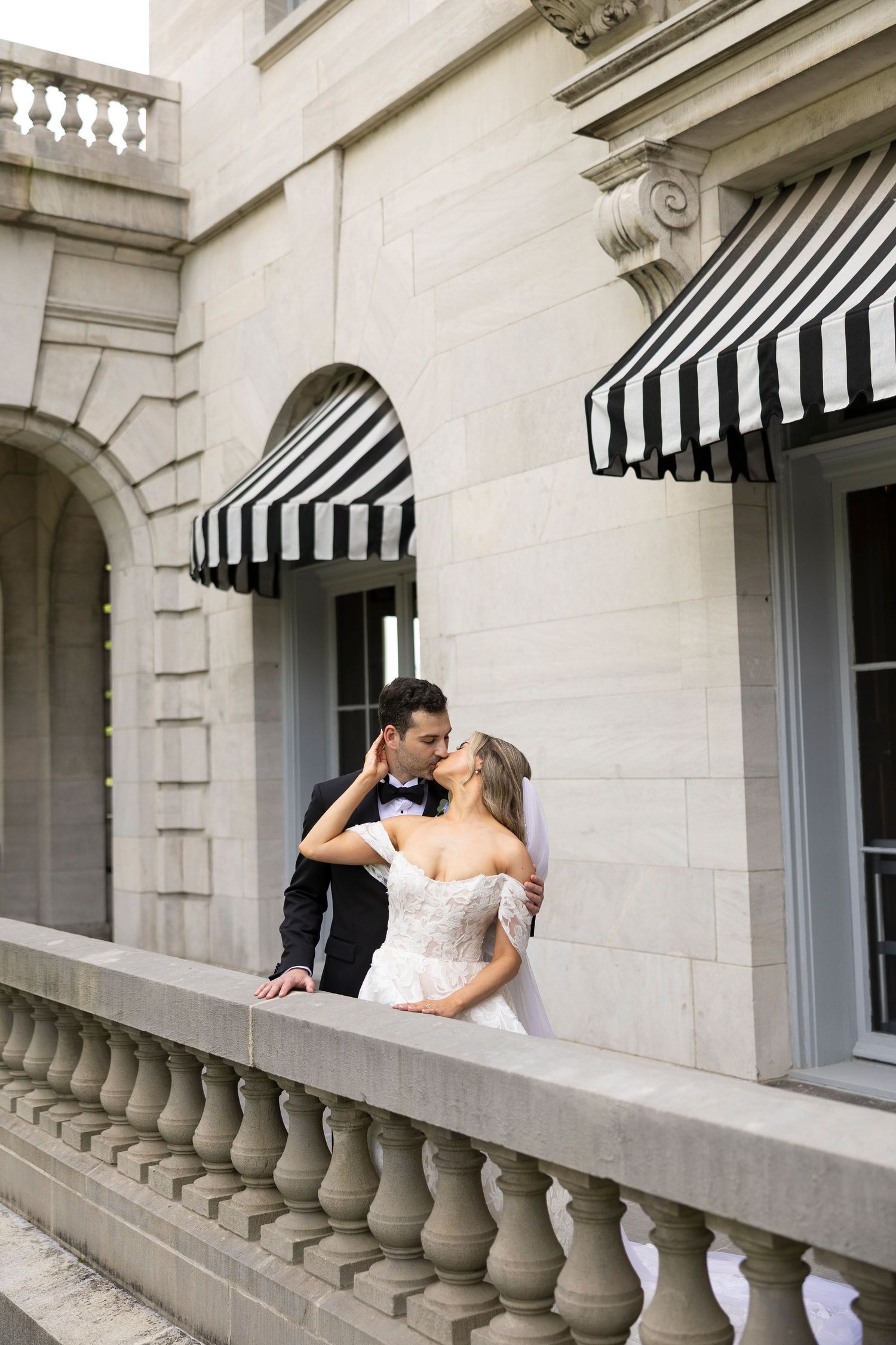 Romantic moment captured on stone balcony with classic black and white striped awnings.