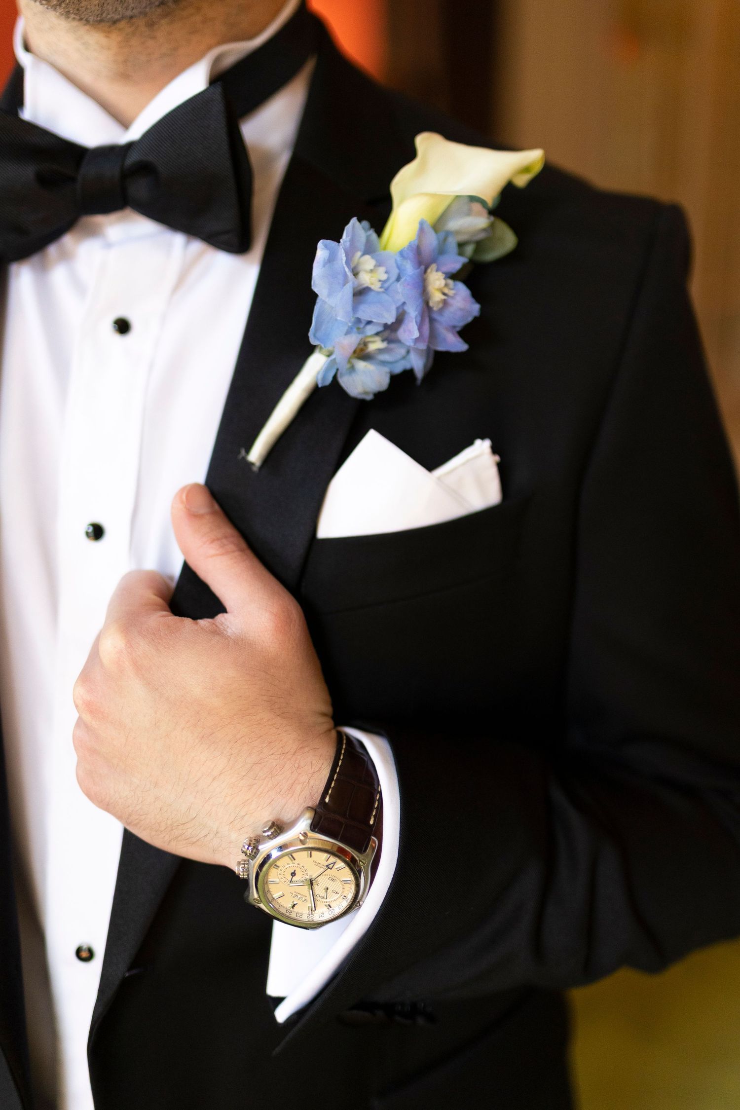 Close-up details of a groom's formal attire showing blue floral boutonniere and black bow tie.