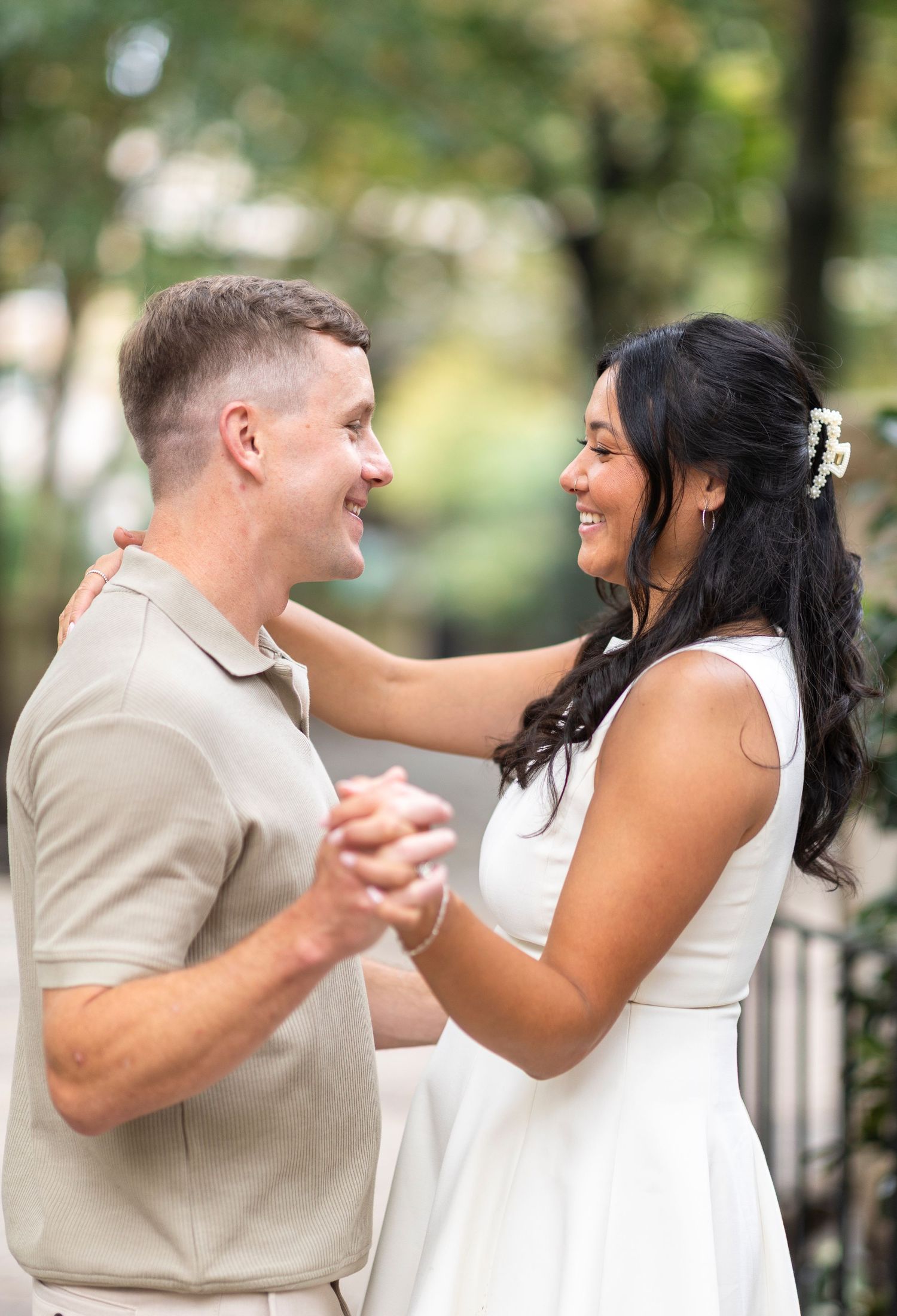 A couple shares joyful laughter together during an outdoor photoshoot in white and beige attire.