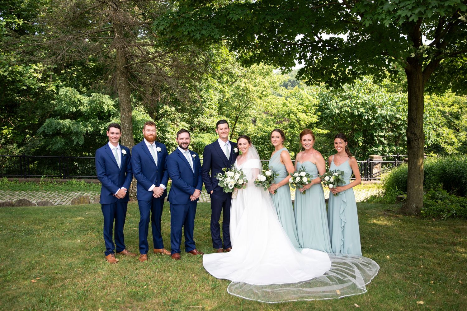 Wedding party members in navy and light blue attire pose together outdoors.