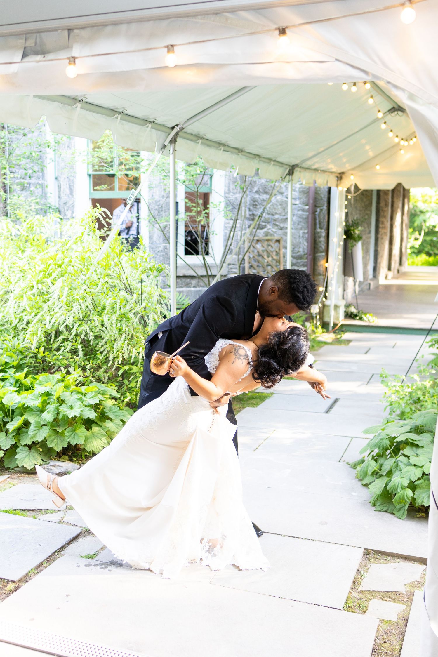 Newlyweds share a romantic dip under a white tent with string lights.