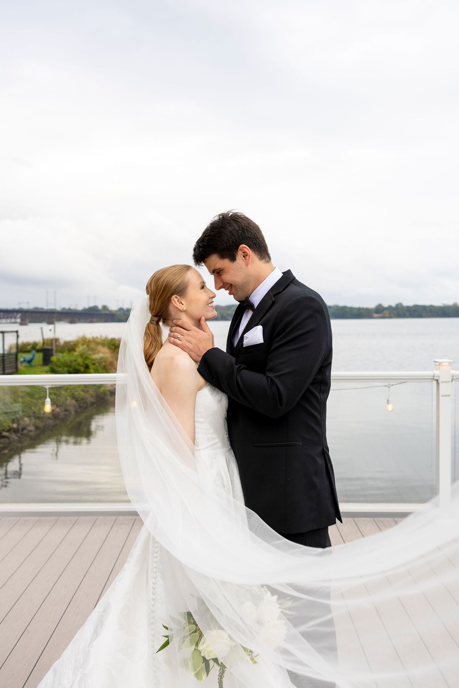 A romantic moment captured with a flowing veil on a waterfront deck.
