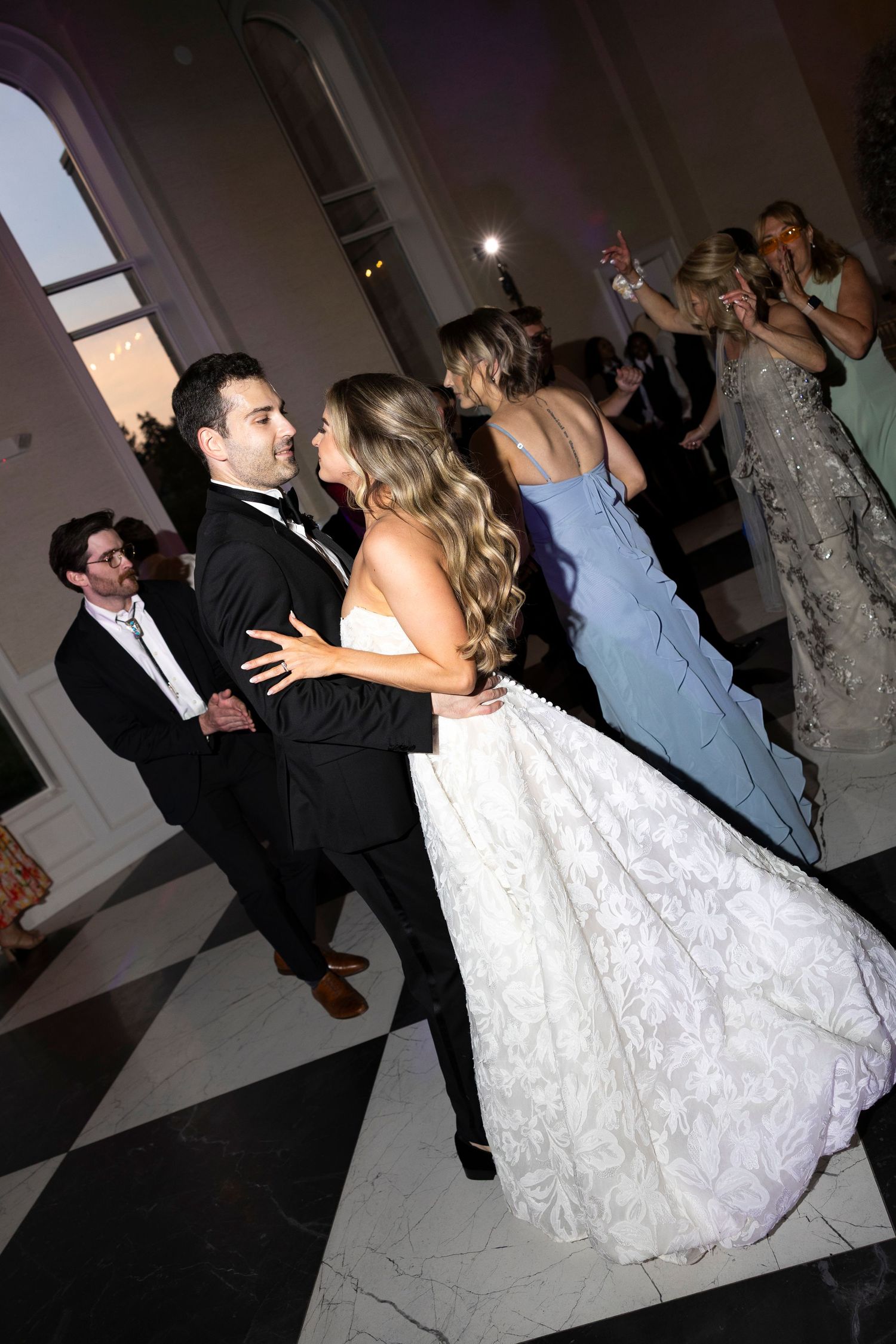 Wedding guests dancing during evening reception celebration.