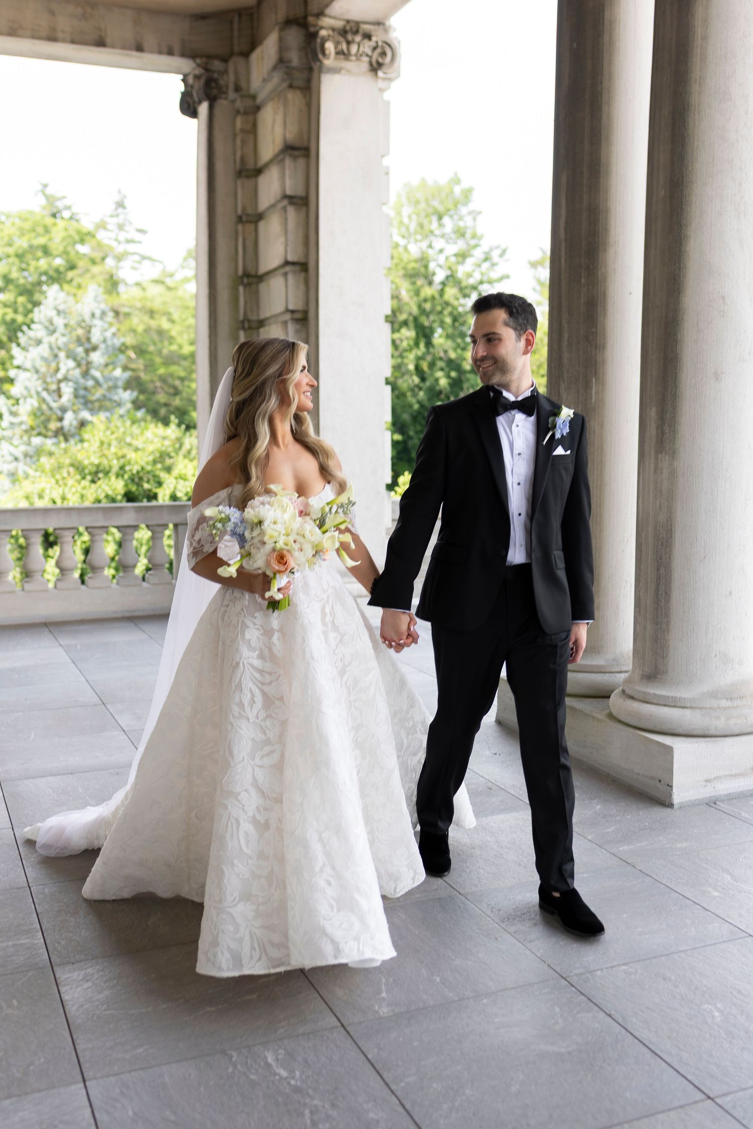 Wedding couple walks together along a grand columned terrace.