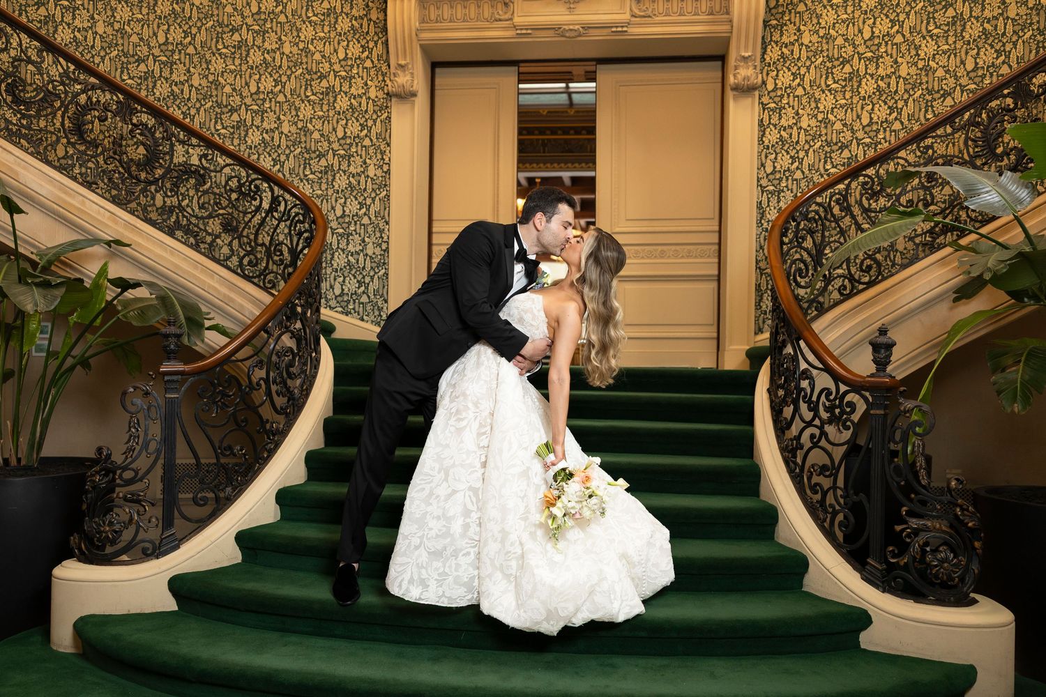 Couple sharing romantic moments on grand staircase with ornate decor.