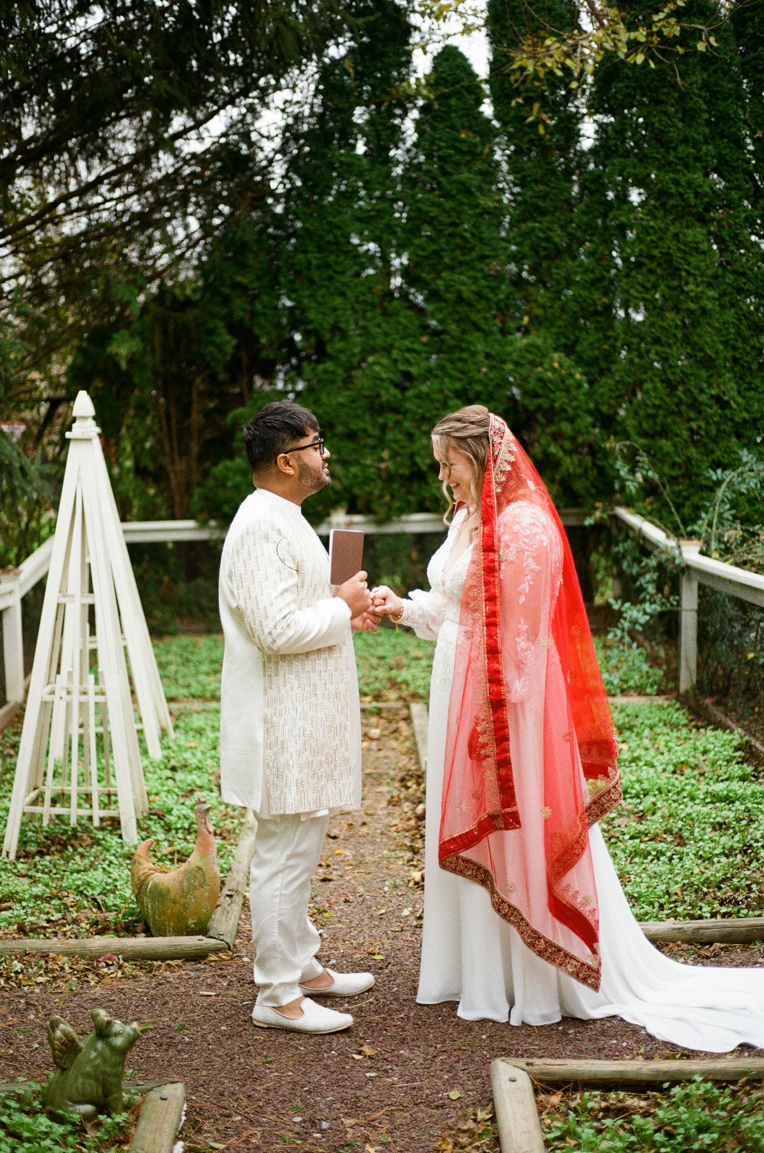 Traditional Indian wedding ceremony with couple in white and red attire outdoors.