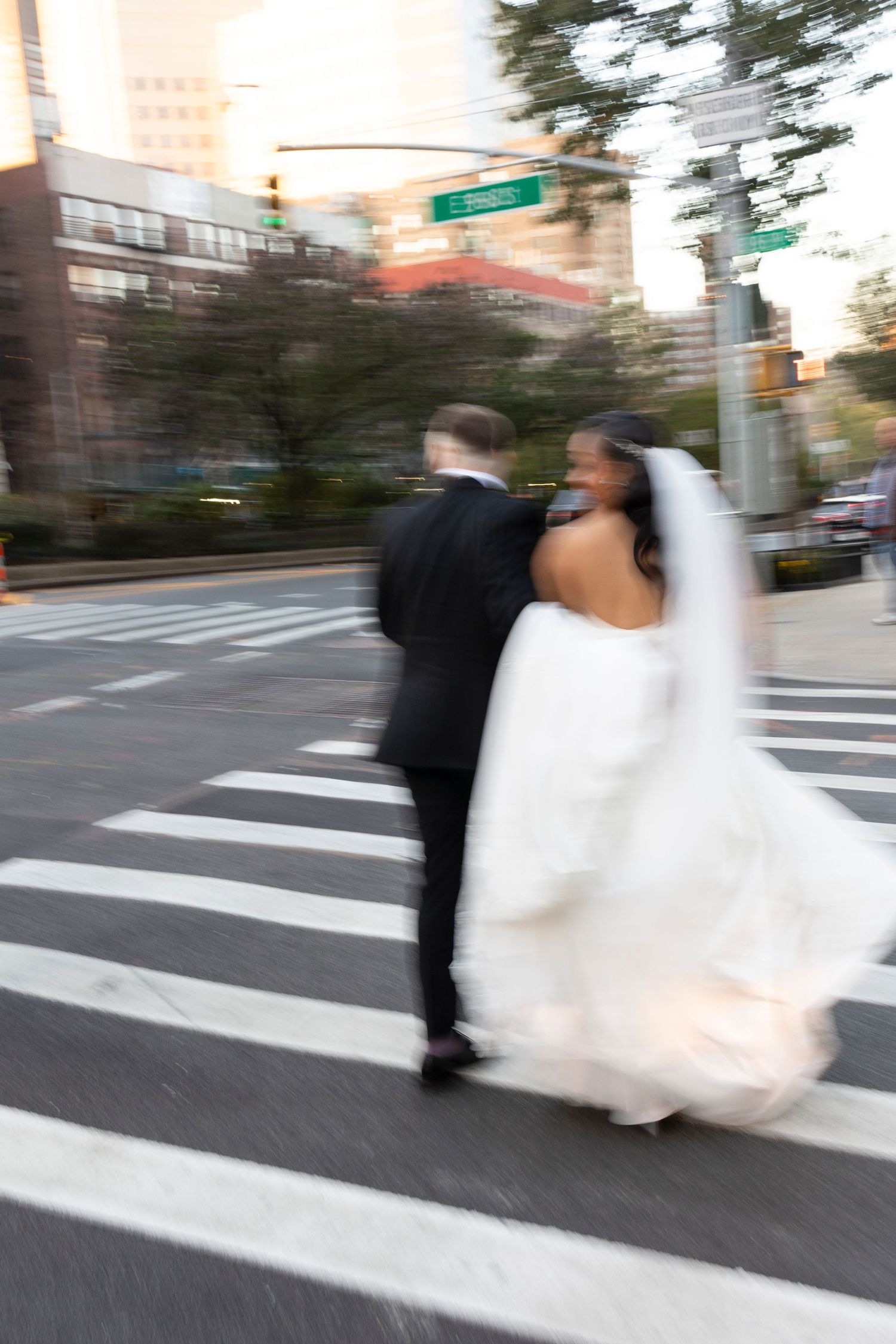 Motion-blurred photograph of wedding couple crossing urban intersection.