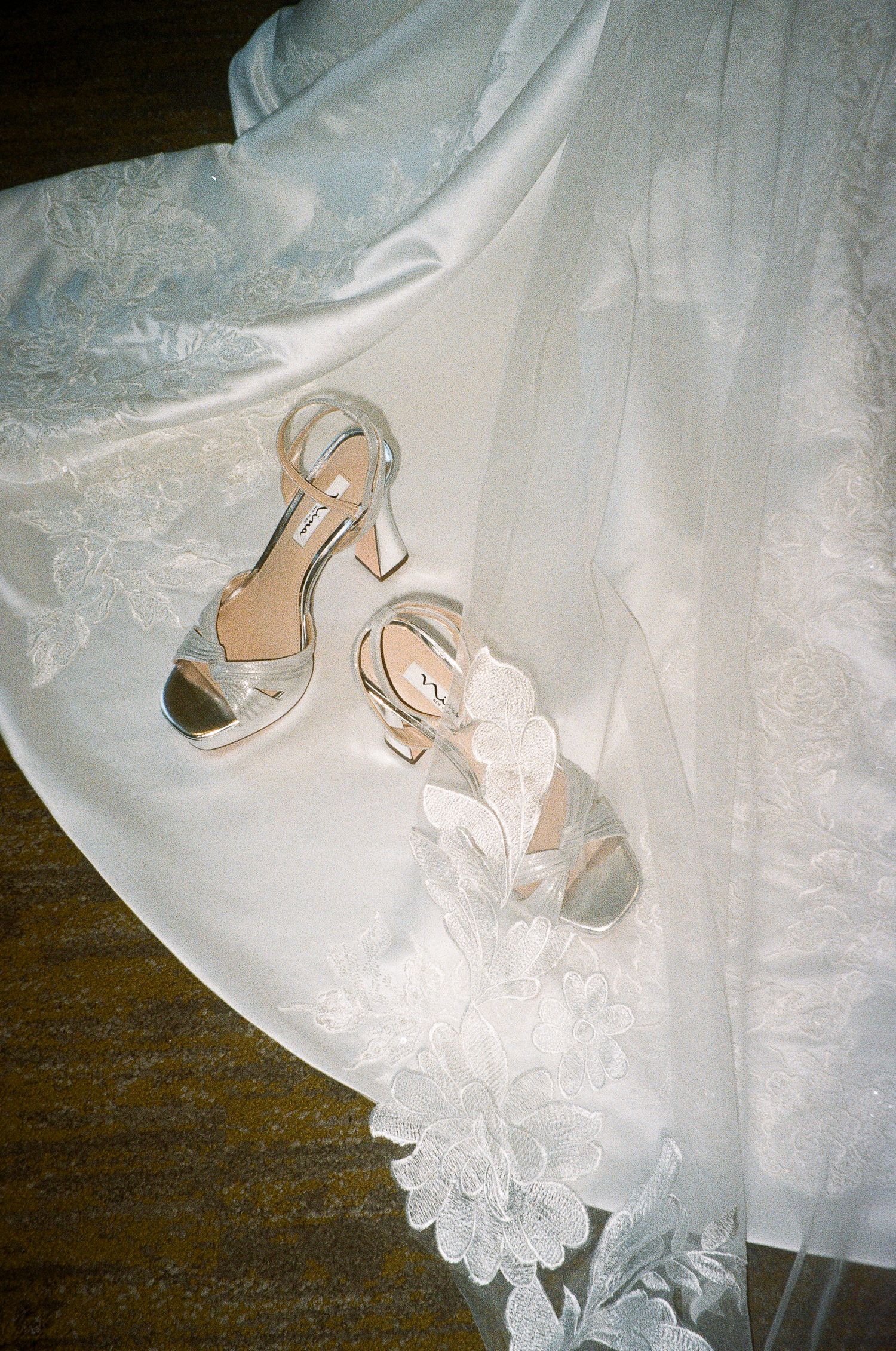 Silver wedding heels resting on delicate white lace wedding dress fabric.