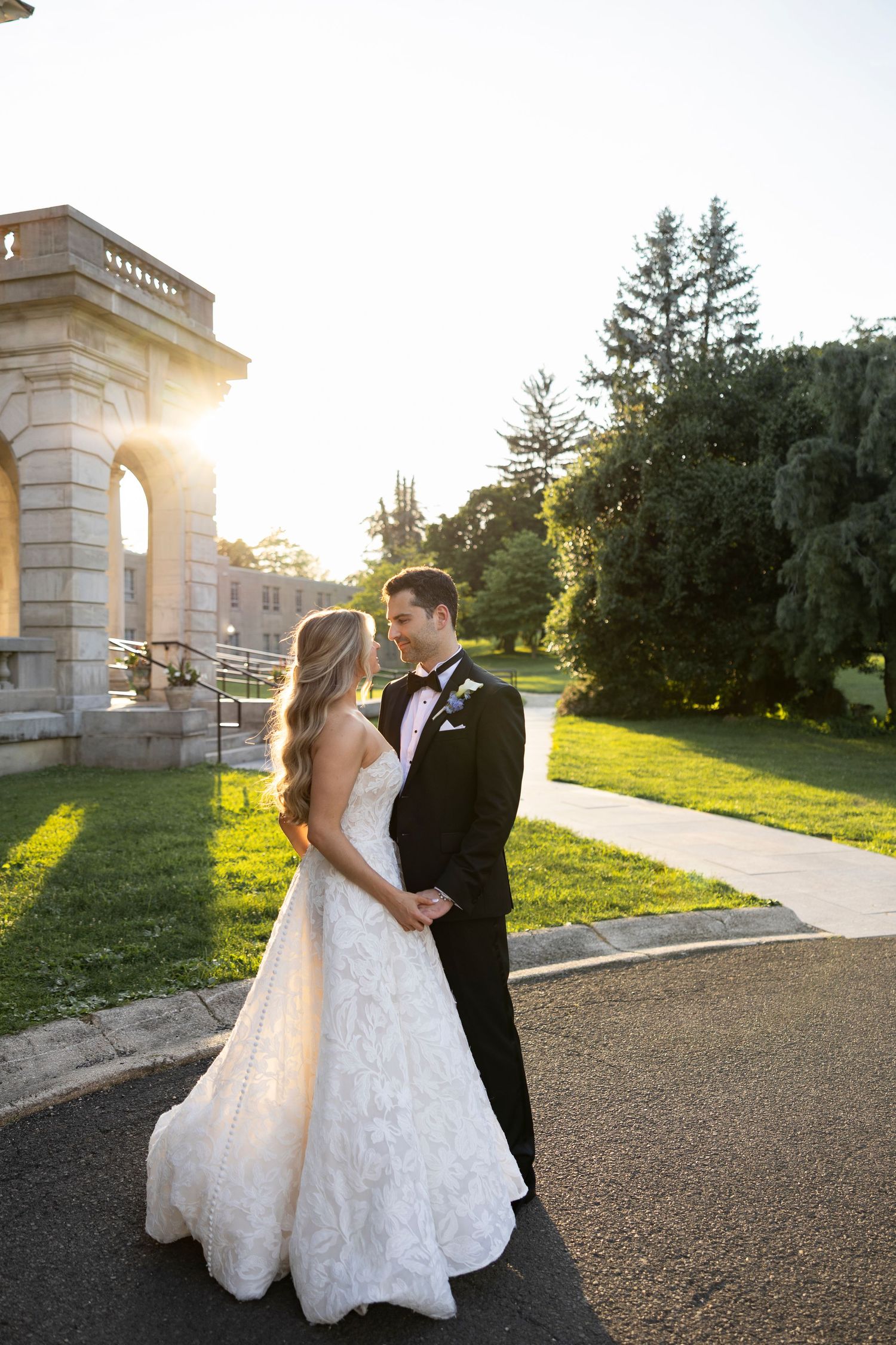 Newlyweds share romantic moments at sunset near a stone architectural feature.