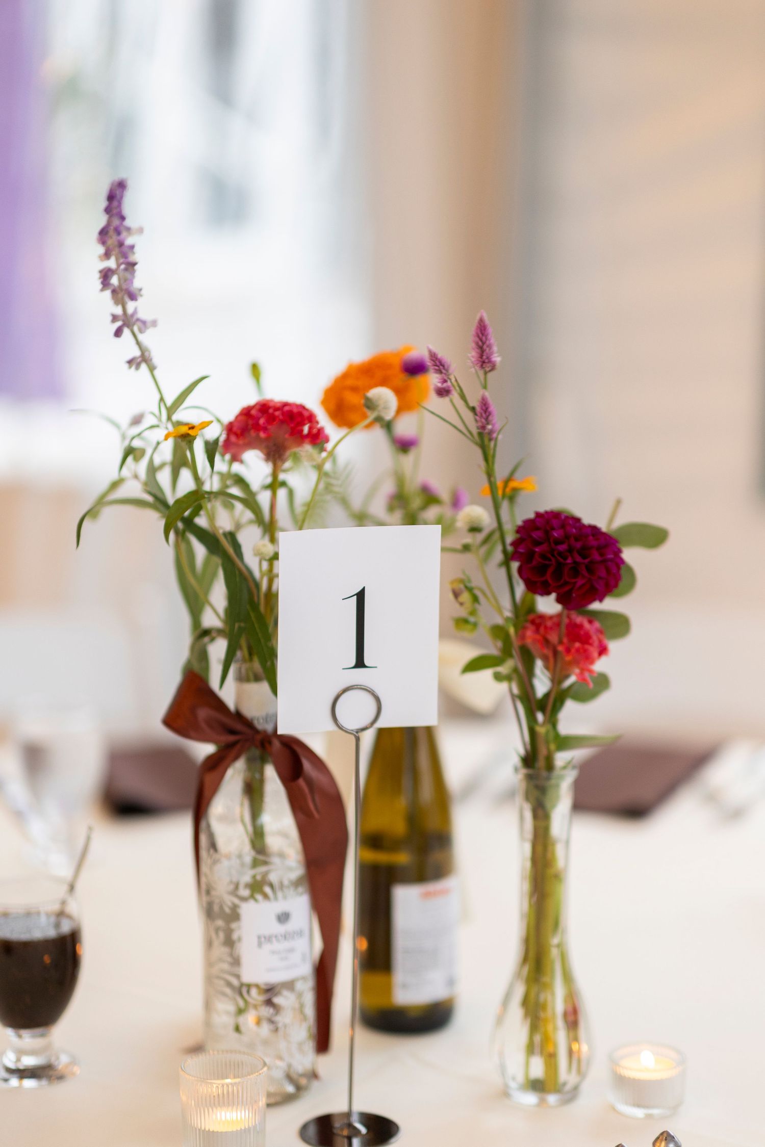 Elegant table settings with numbered cards and fresh flower arrangements in glass bottles.