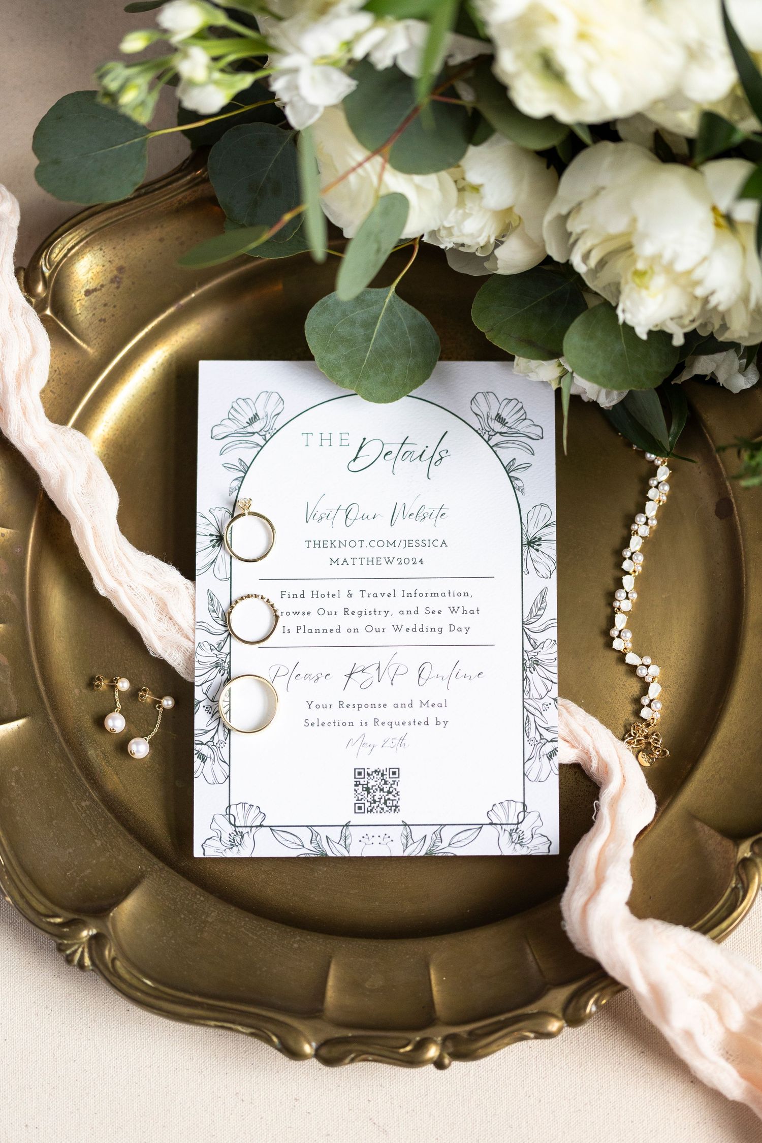 Wedding invitation on gold charger plate with white flowers and eucalyptus leaves.