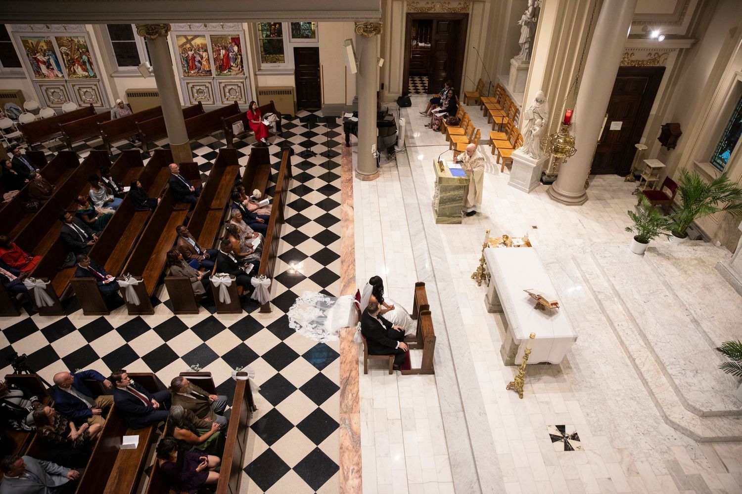 Wide angle view of wedding ceremony in progress inside historic church with checkered floor.