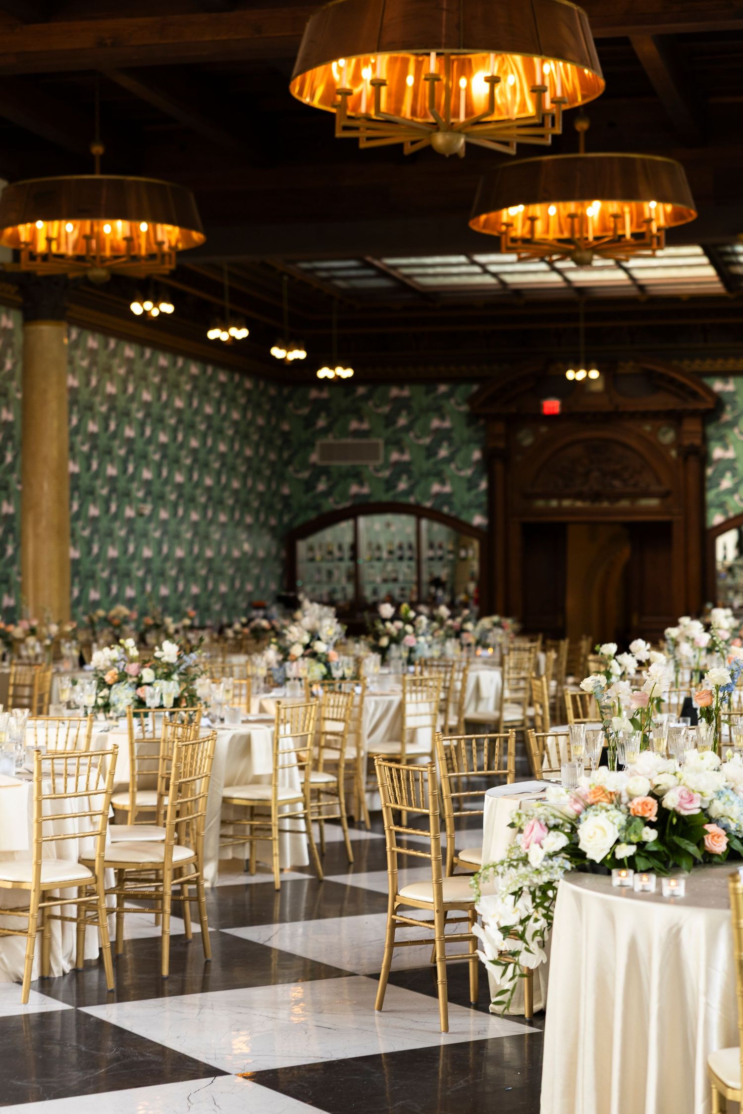 Elegant wedding reception ballroom with gold chairs and white floral centerpieces.