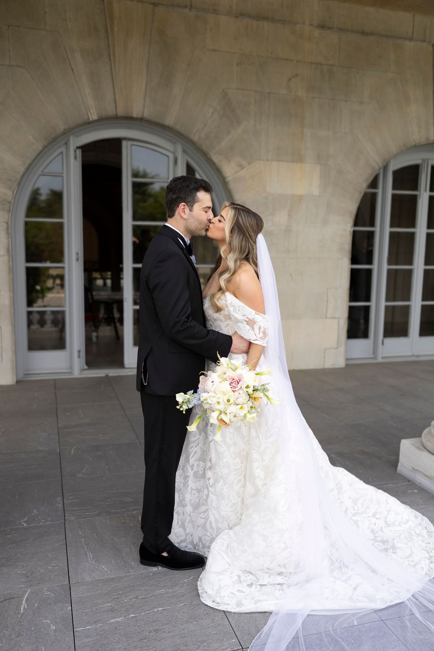 Newlyweds share their first kiss in an elegant stone archway setting.