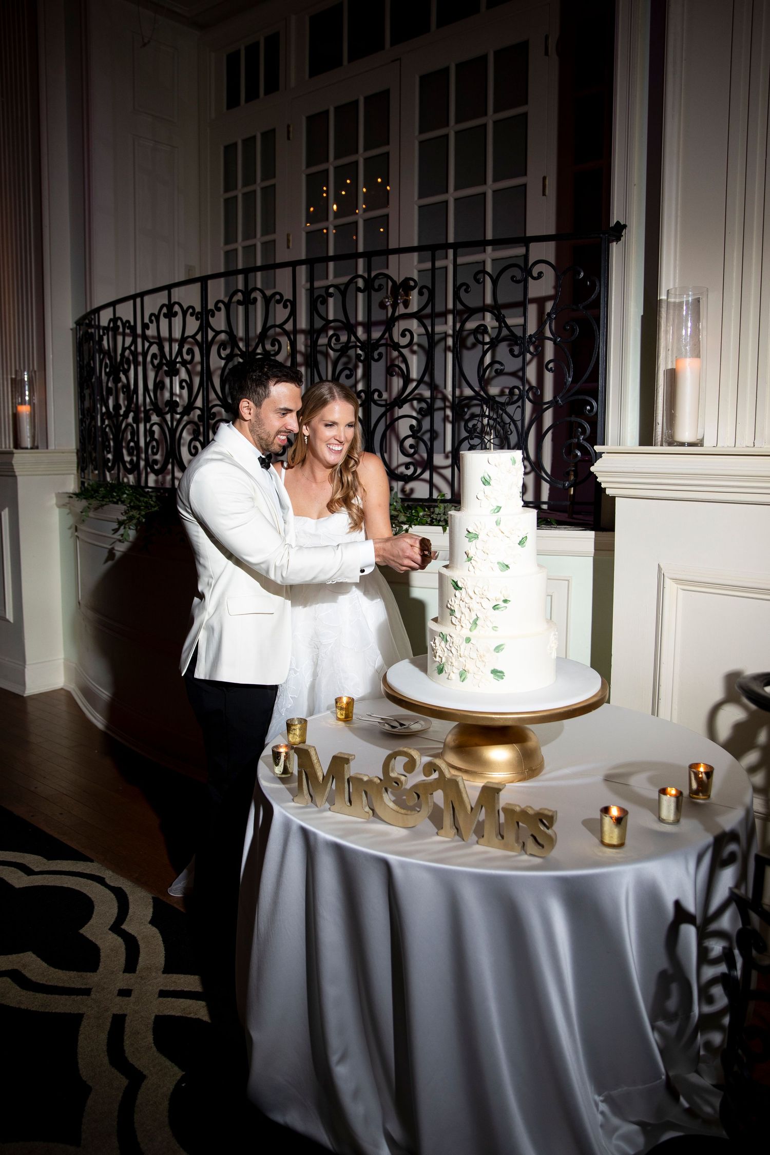 Bride and groom cutting their white three-tier wedding cake at a elegant reception with Mr & Mrs sign.