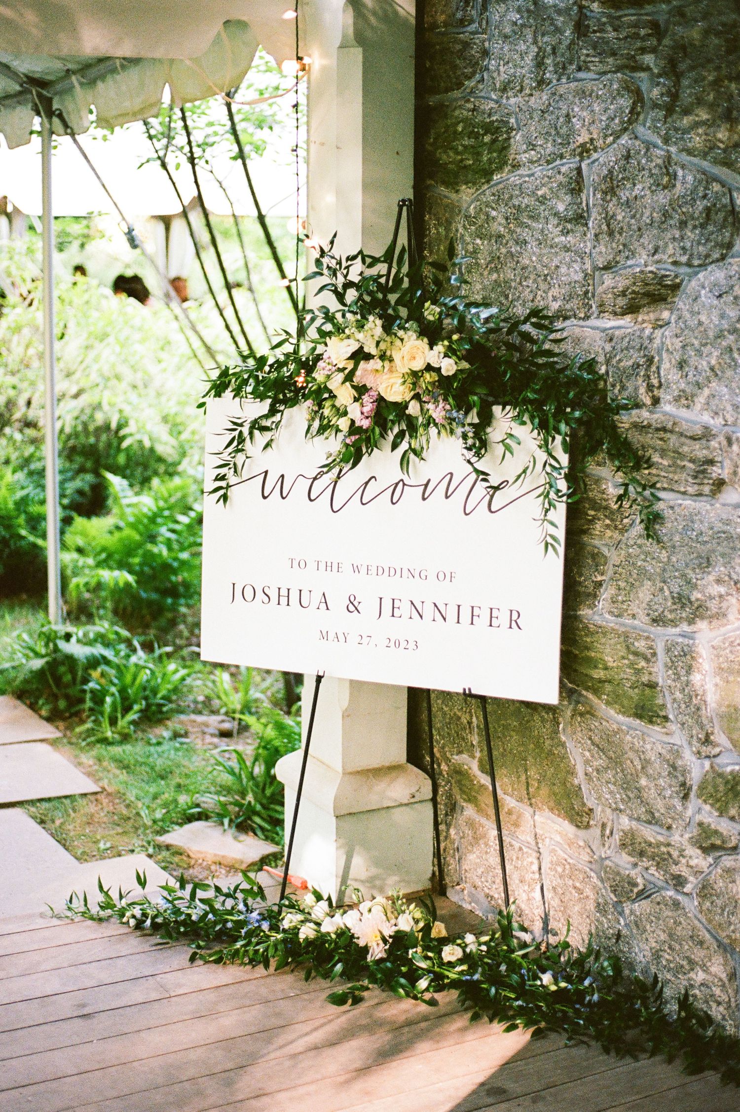 Elegant wedding welcome signs displayed against a rustic stone wall with greenery.