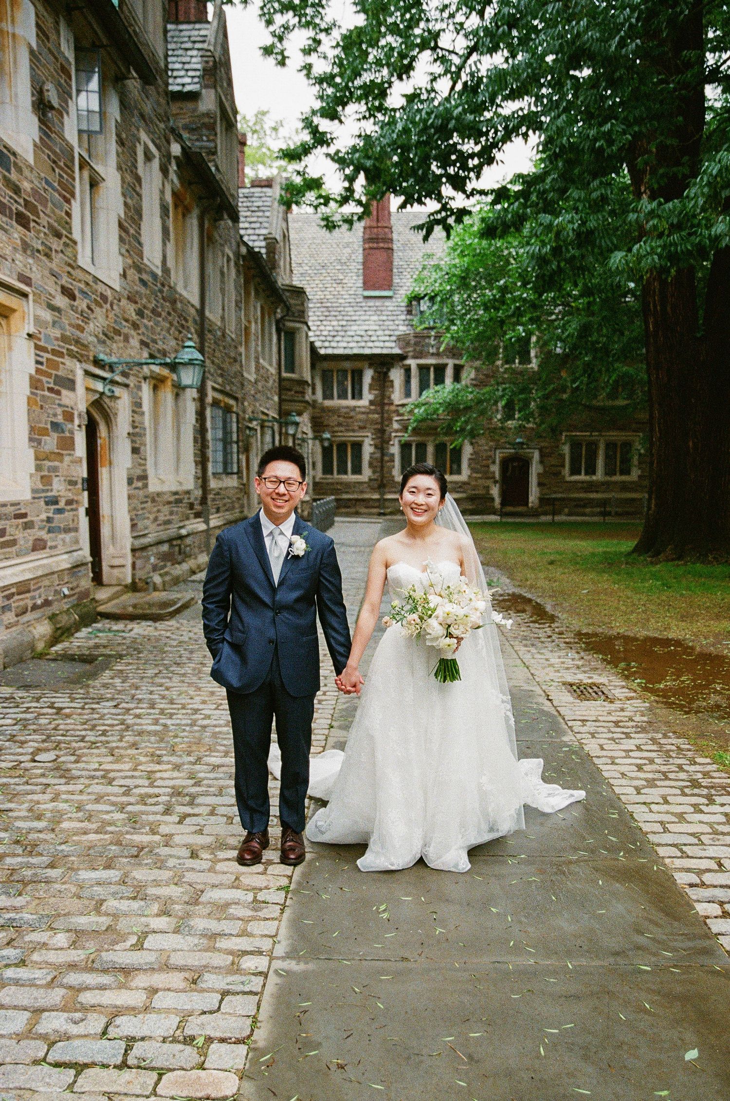 A wedding couple walking along a cobblestone path beside historic stone buildings.