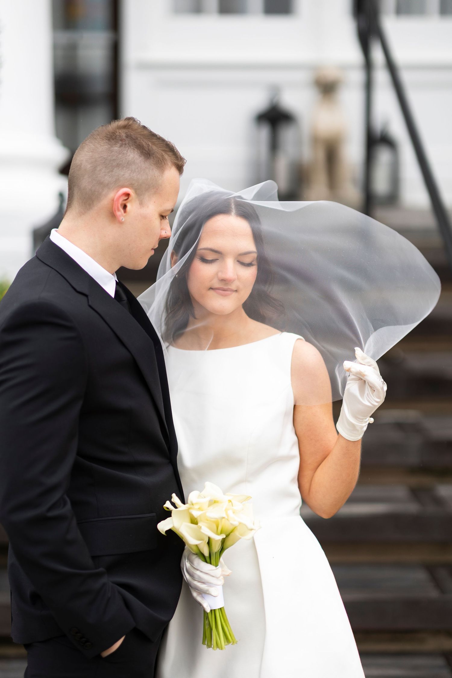 A bride in a classic white dress holds a bouquet while her veil flows in the wind.