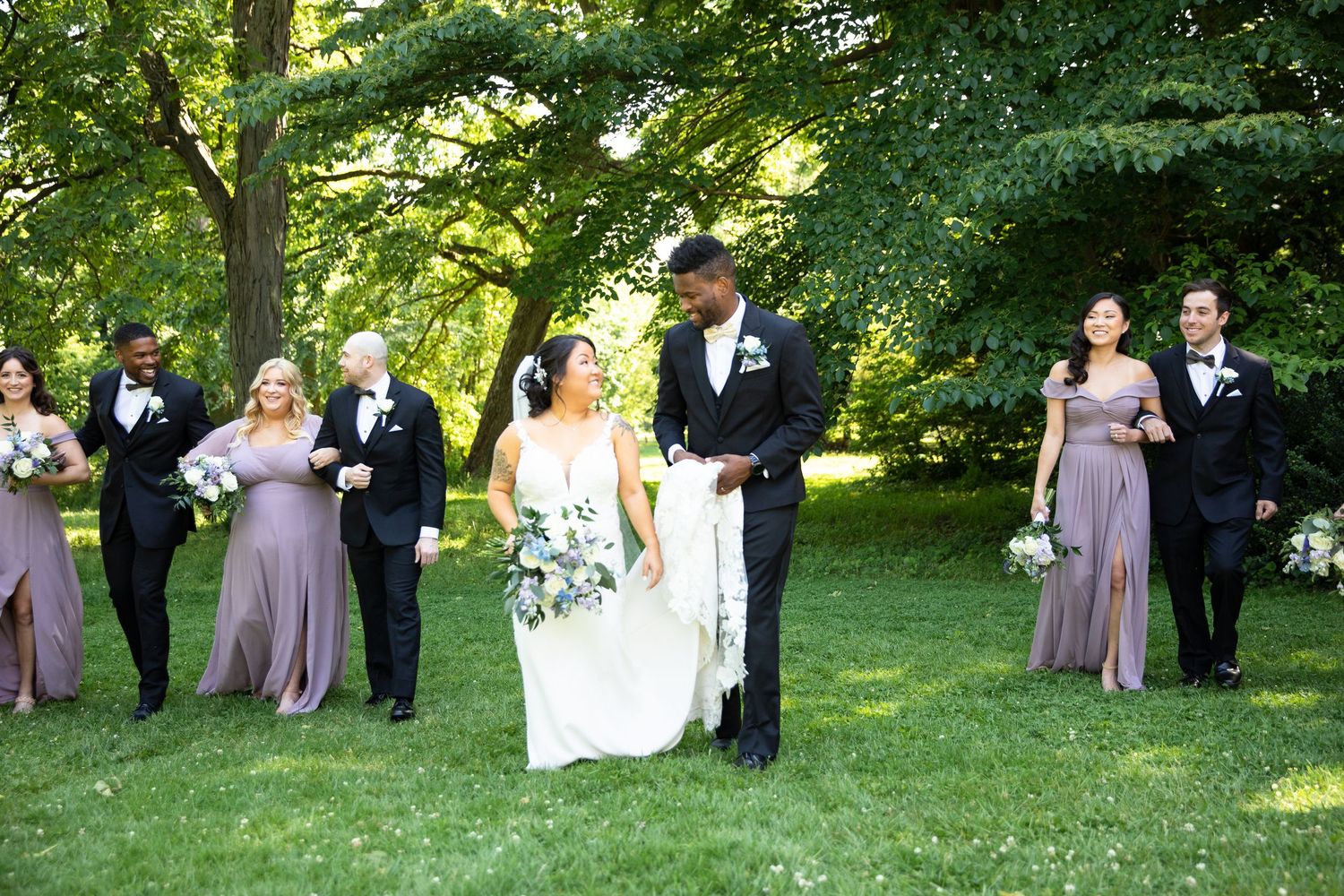 Wedding party arranged in formal poses outdoors under green summer foliage.