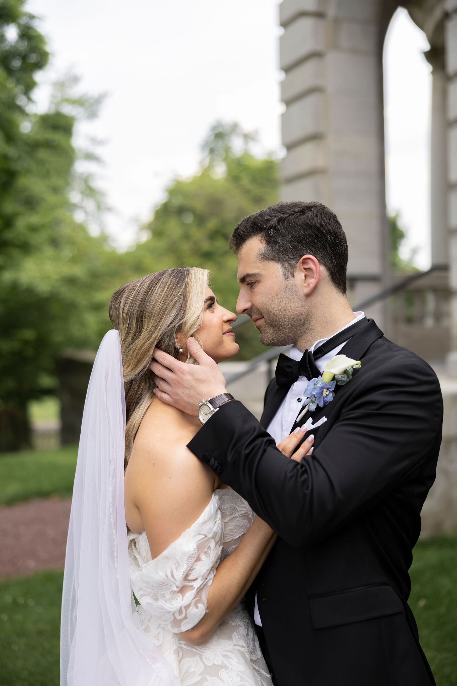 Intimate wedding portrait captured under stone colonnade with soft natural lighting.
