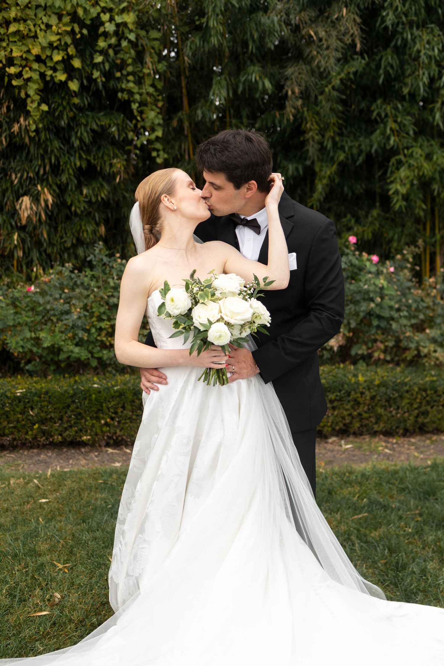 A romantic wedding moment captured in a garden setting with white florals and formal attire.