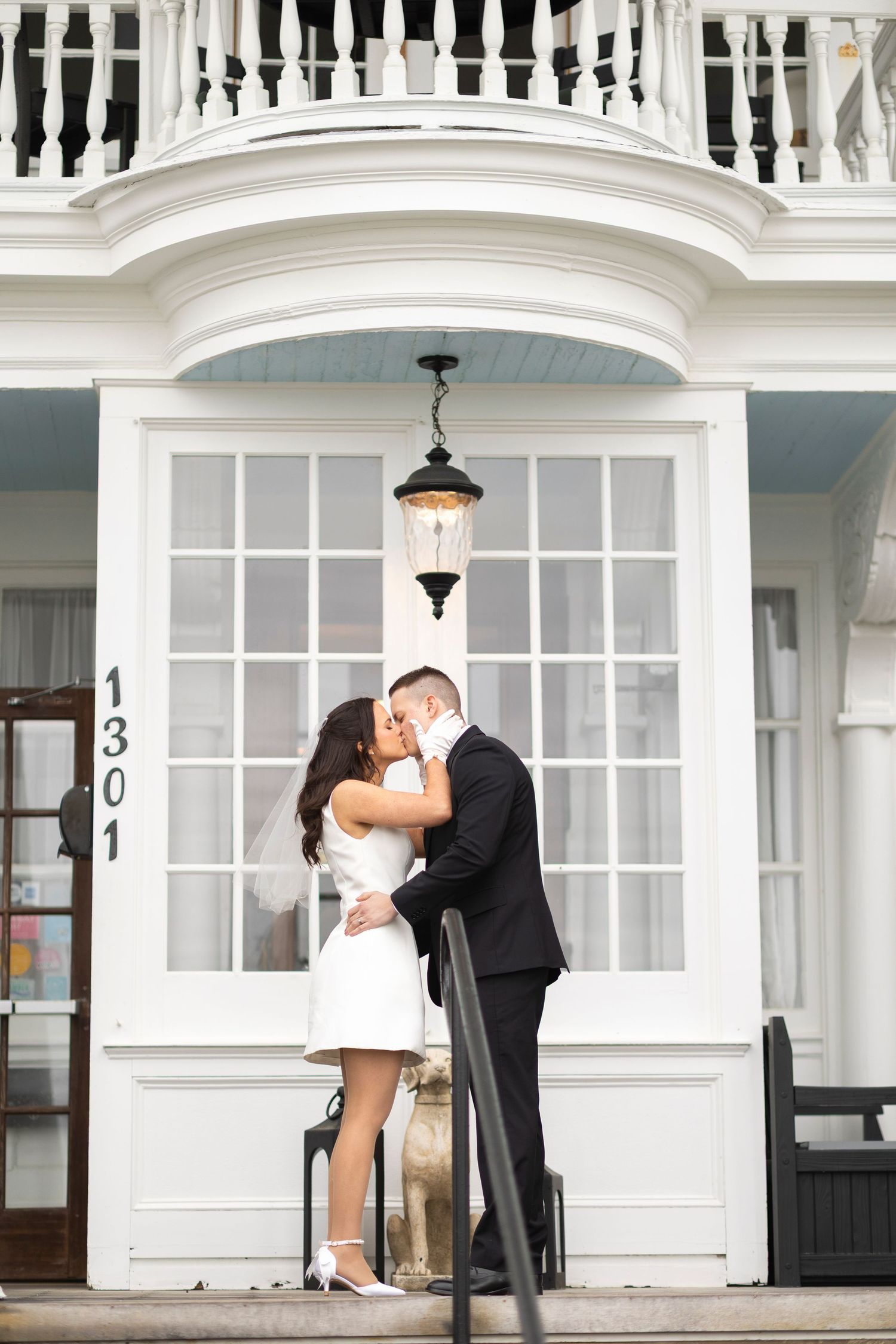 Couple embracing outside white colonial building with elegant architectural details.