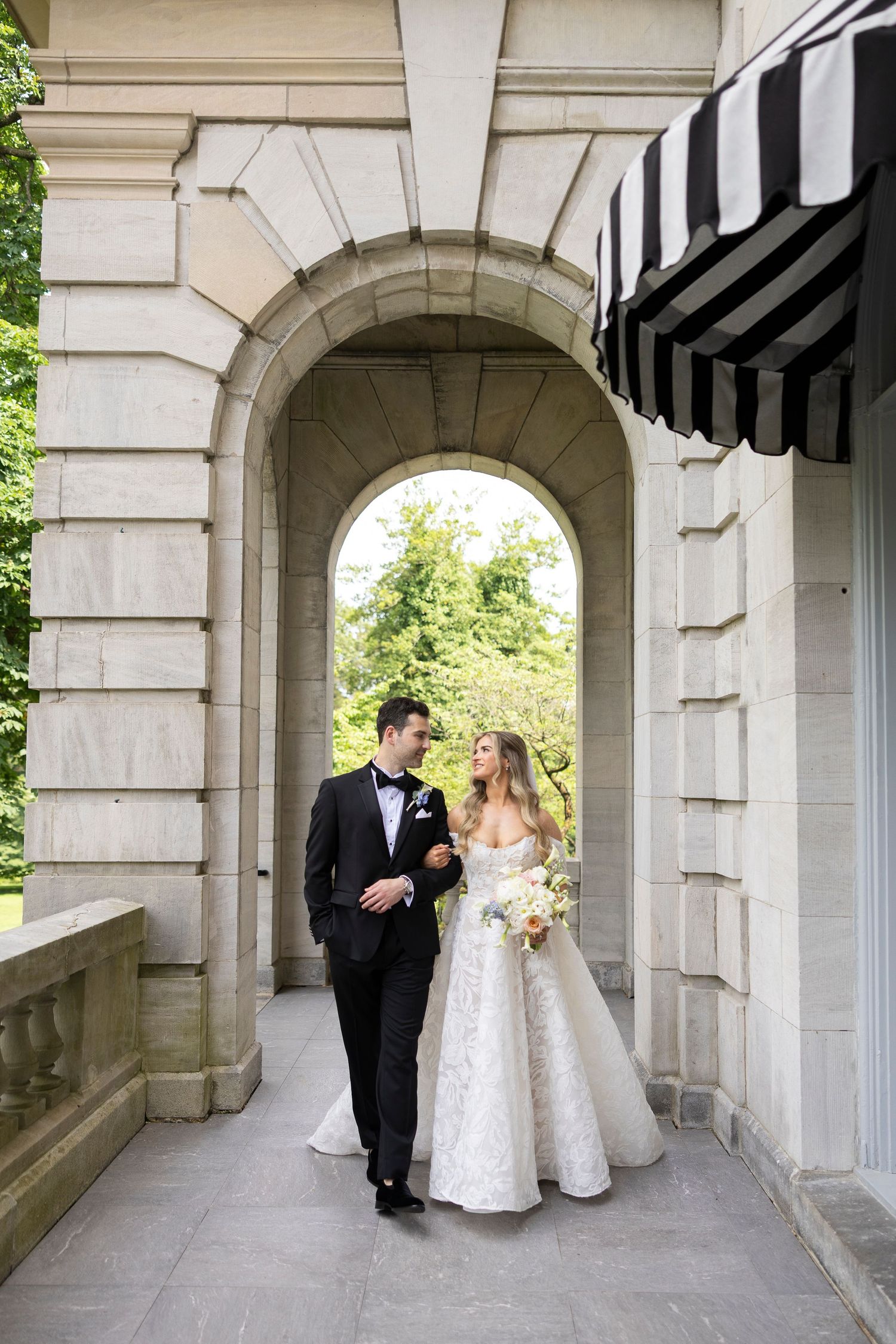 A classic wedding portrait under a stone archway with black and white striped awnings.