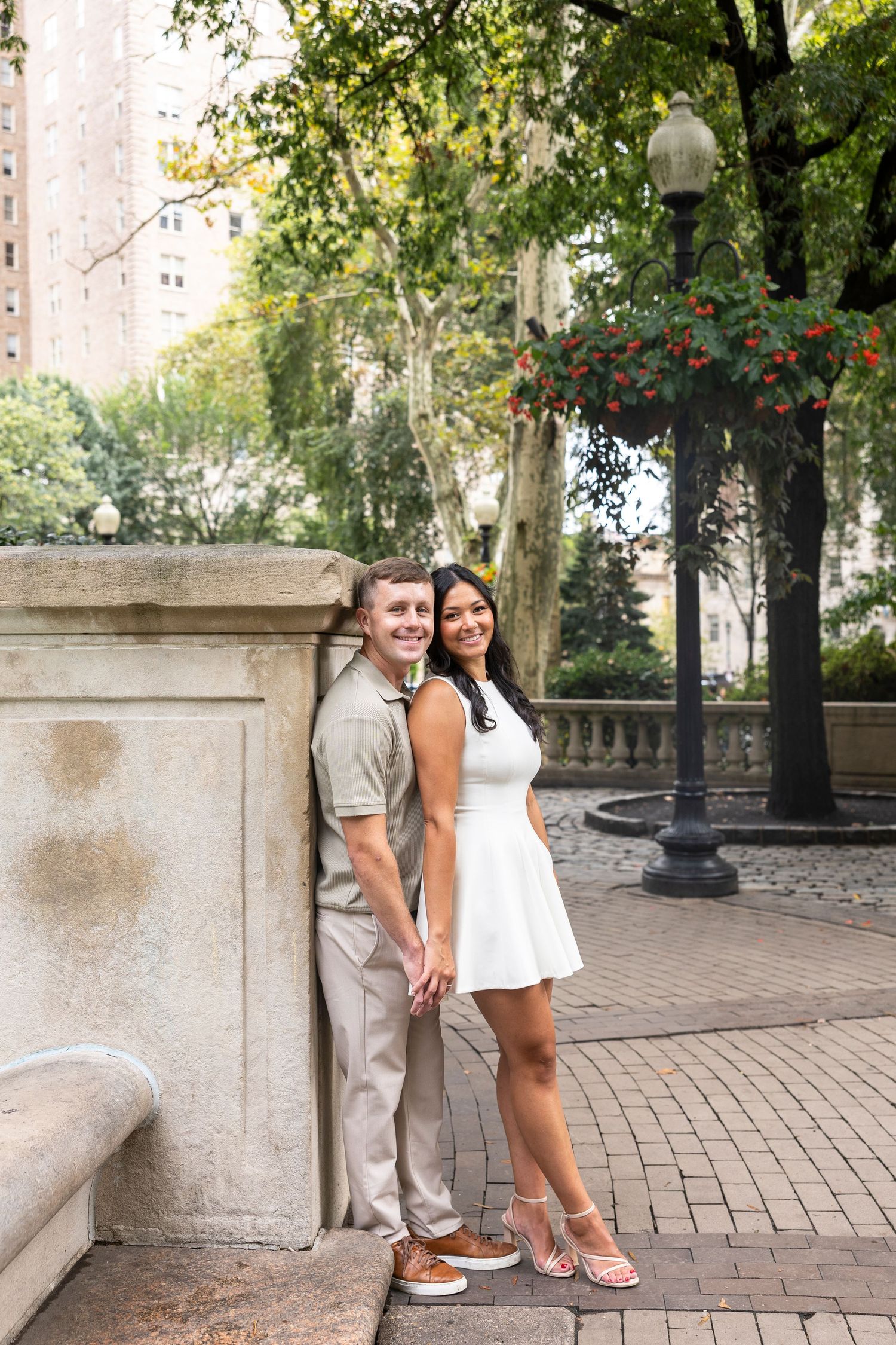 A couple shares a romantic moment against a stone wall in a park setting.