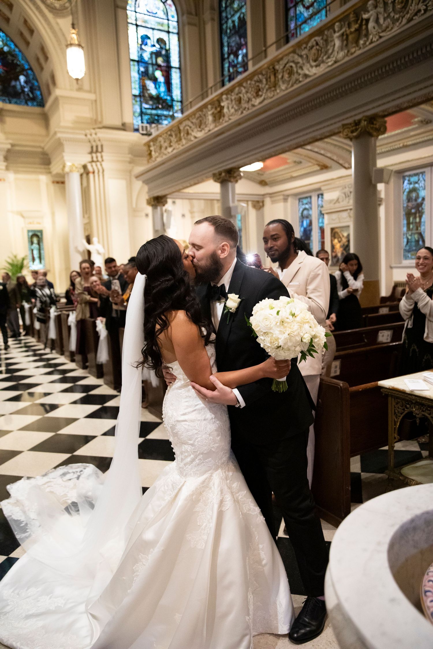 Wedding couple shares romantic moments in a grand church with stained glass windows and checkered floors.