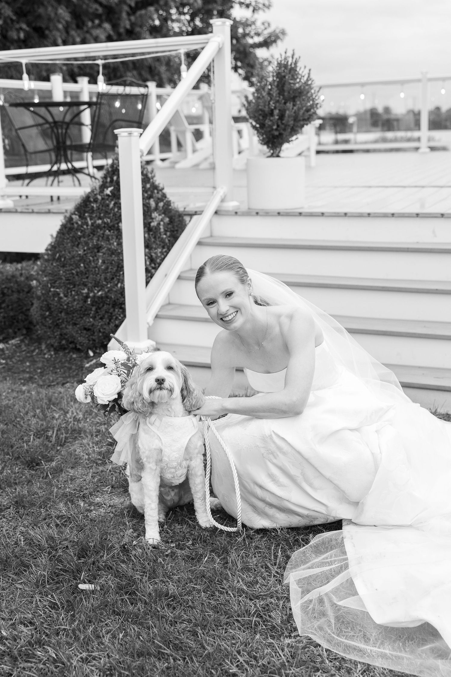 A bride in her wedding gown poses with her fluffy white dog on outdoor steps.