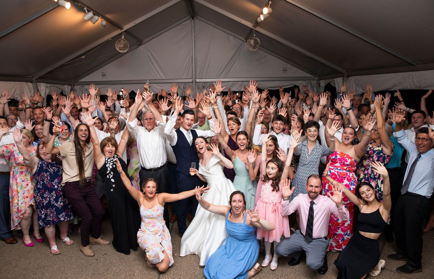 Wedding guests dance with raised arms during a lively reception celebration.