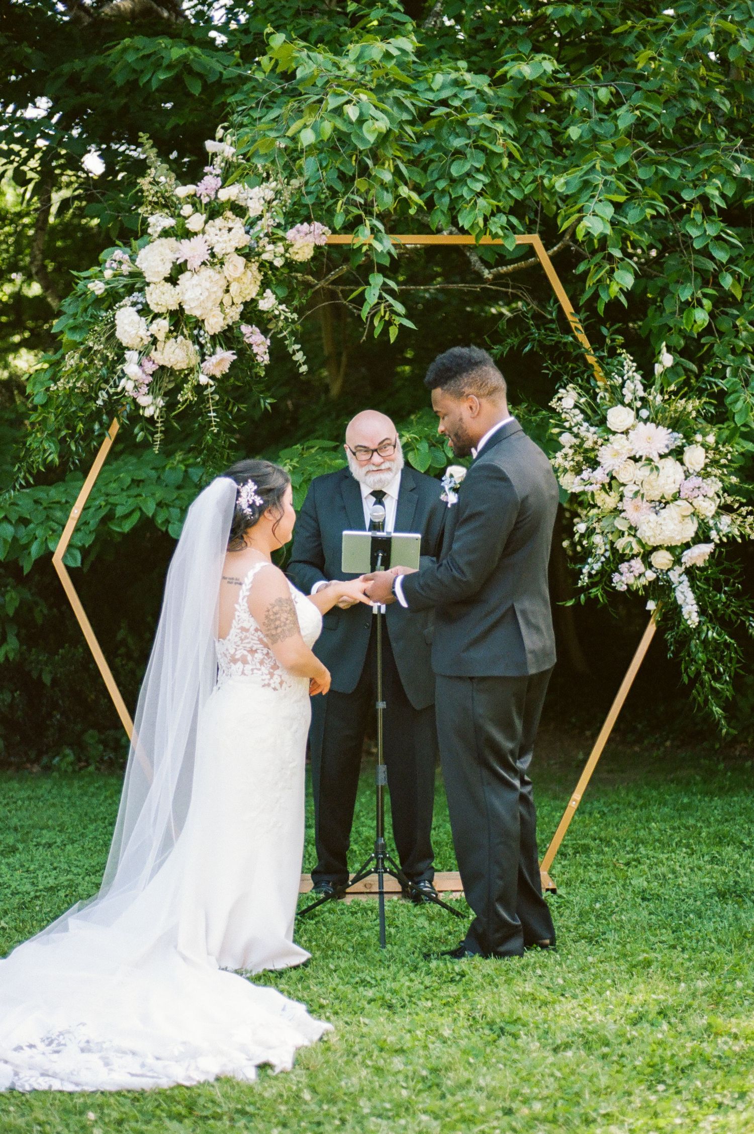 Outdoor wedding ceremony under wooden hexagon arch decorated with white flowers.