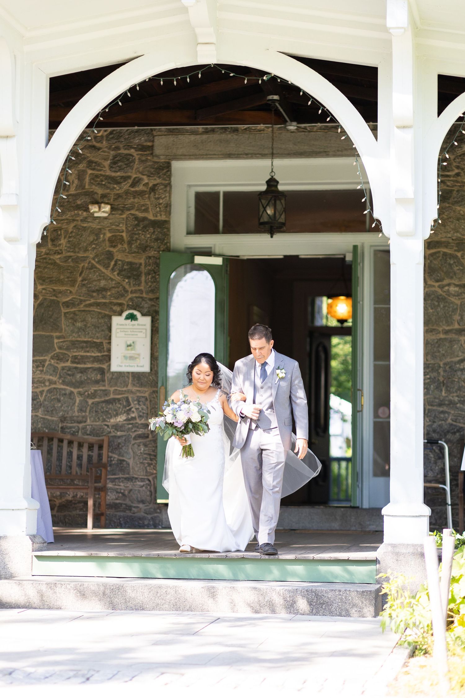 Wedding couple and party members pose under a stone building's white columned porch.