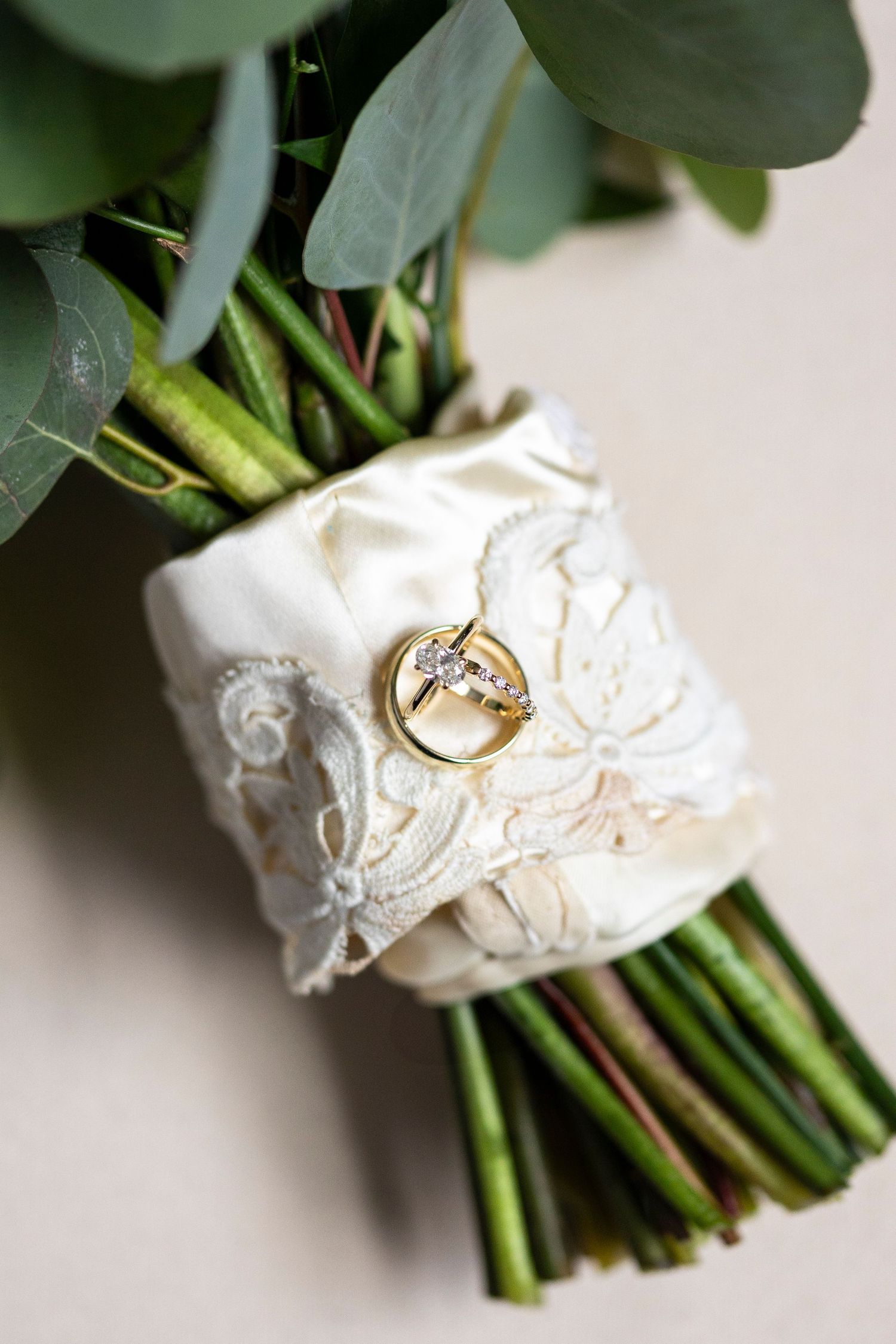 Wedding ring photographed on white lace bouquet wrap with green stems.
