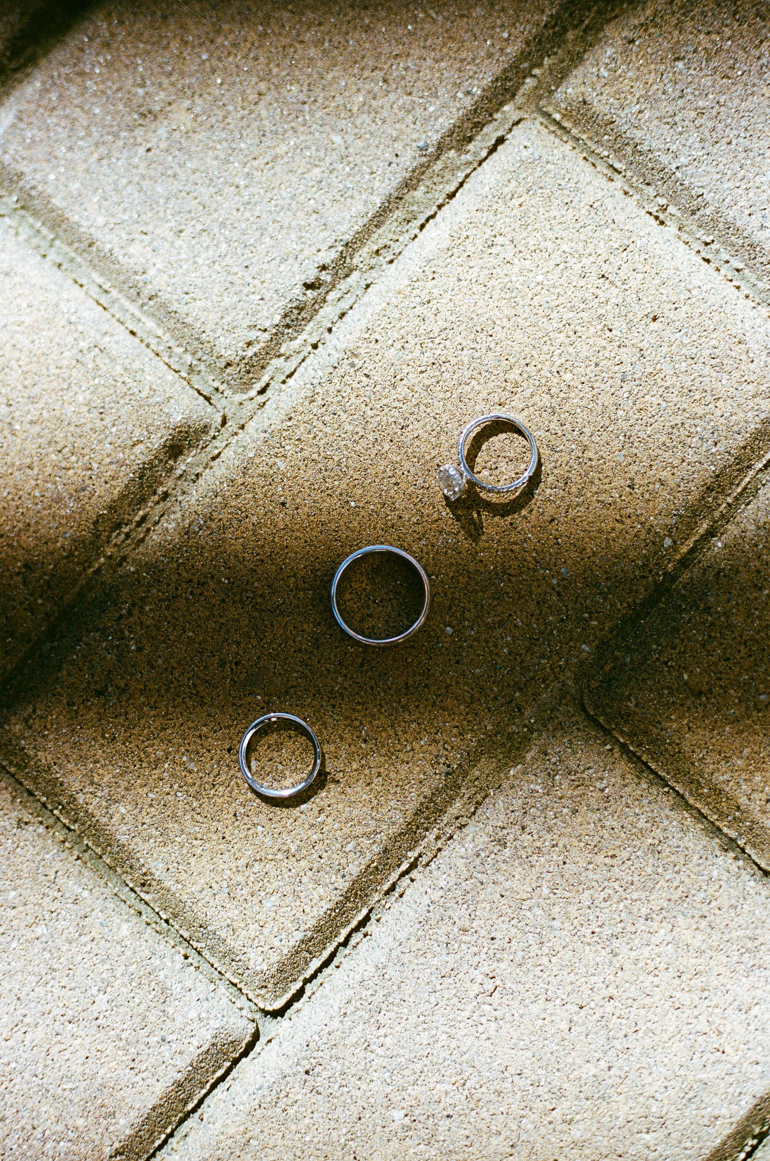 Wedding rings photographed on textured beige surface with diagonal shadows.