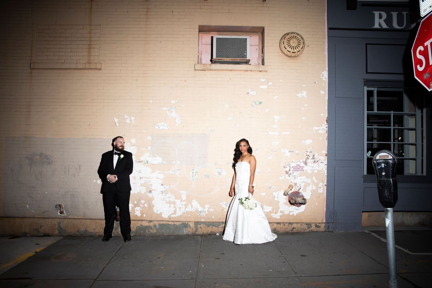 Dramatic wedding photo against minimalist beige wall in urban setting.