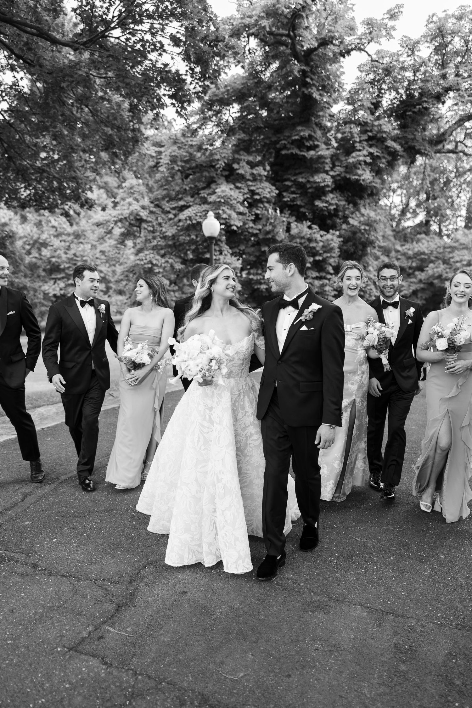 Black and white photo of wedding party walking together on outdoor path.