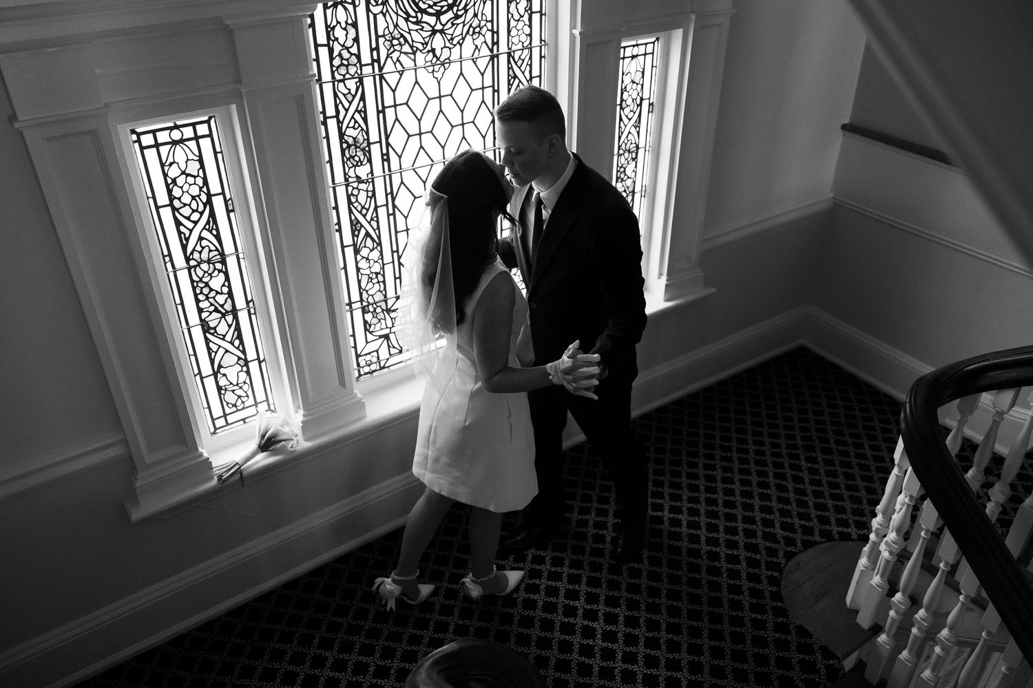 A romantic moment captured on a patterned carpet staircase with decorative windows.