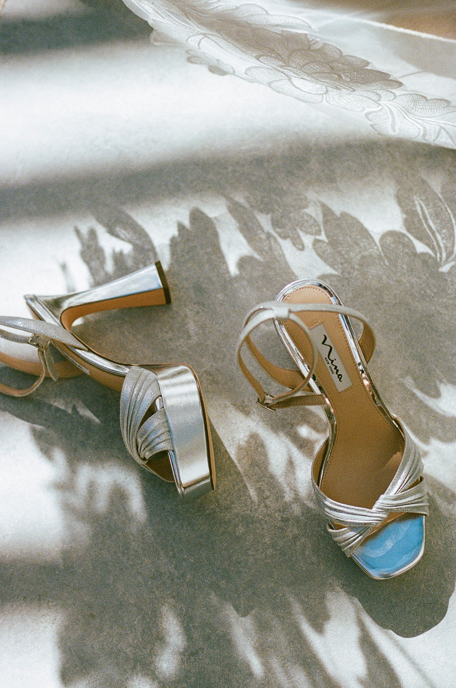 Silver bridal sandals with blue soles photographed against white fabric with dramatic lighting.
