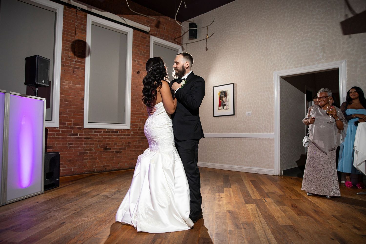 Wedding couple dancing together in an elegant venue with exposed brick and wooden floors.